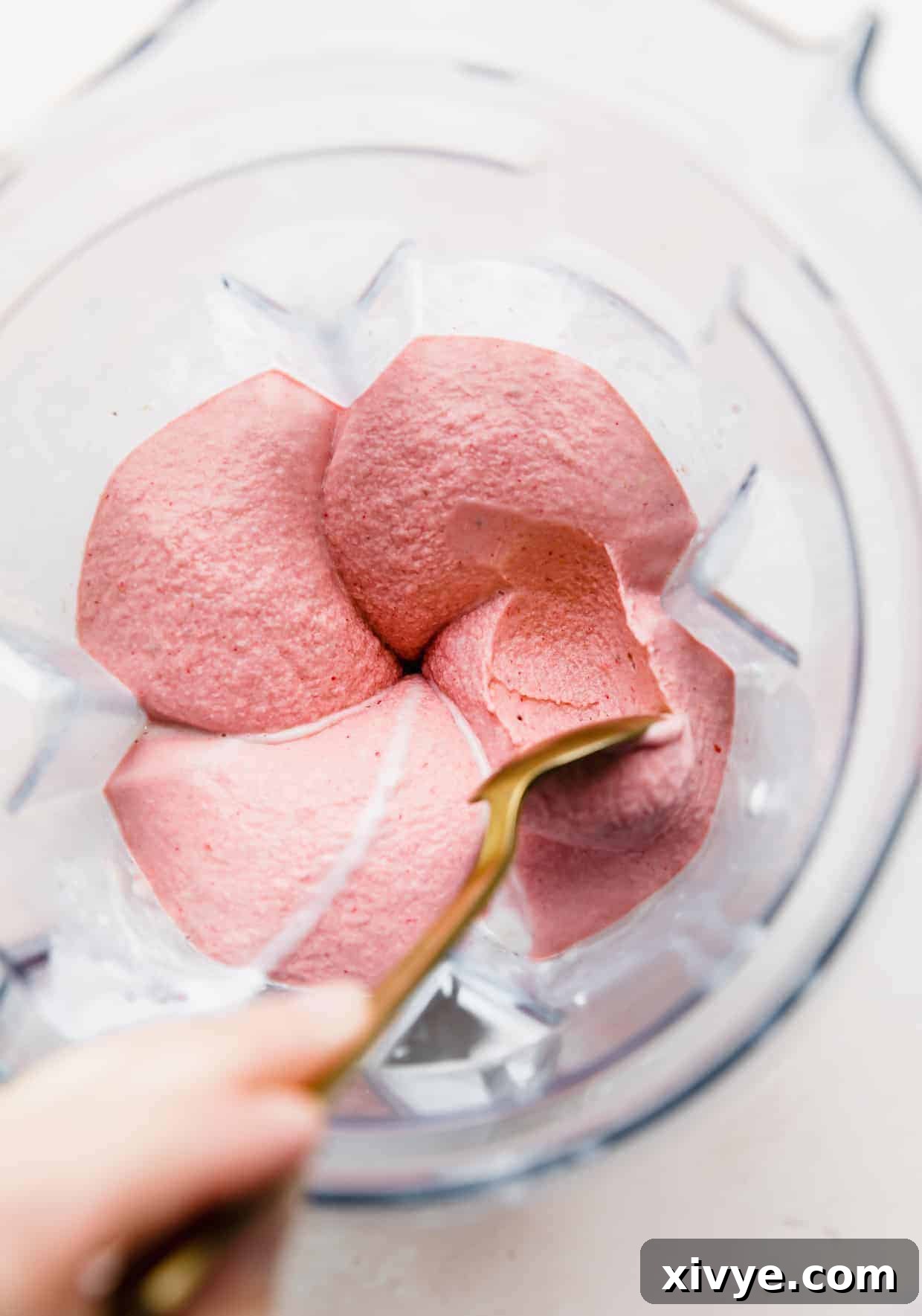 Tropical Strawberry Pineapple Smoothie 7 Overhead photo of a hand holding a spoon scooping out thick Strawberry Pineapple Smoothie straight from the blender.