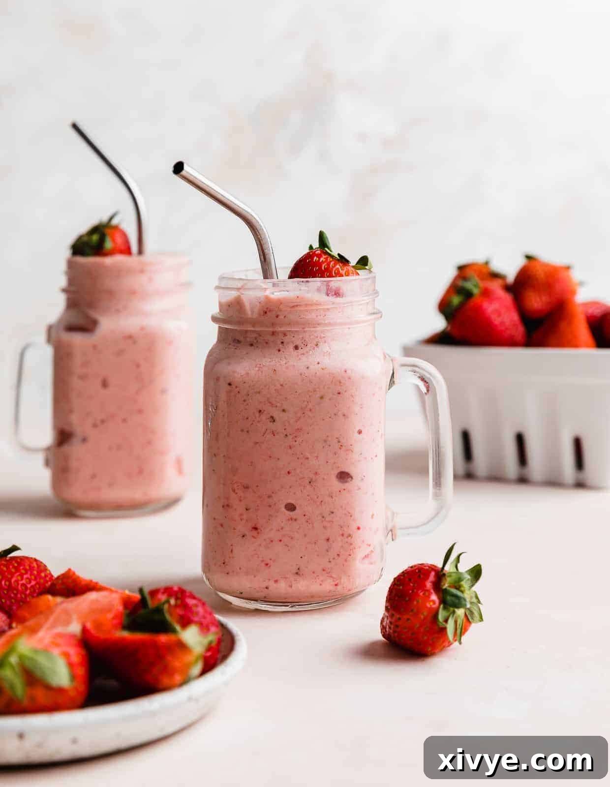 Tropical Strawberry Pineapple Smoothie 8 A pink Strawberry Pineapple Smoothie in a mason glass jar with a metal straw, against a white background with a basket of strawberries near the smoothie.