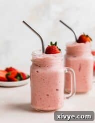 Two mason jar glasses full of Strawberry Pineapple Smoothie with a fresh strawberry resting on the top of the smoothie.