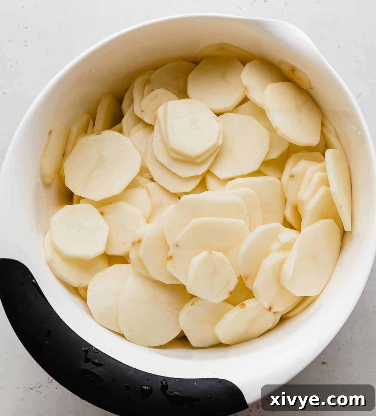 Ultimate Gluten Free Scalloped Potatoes 4 A white bowl full of raw thinly sliced potatoes.