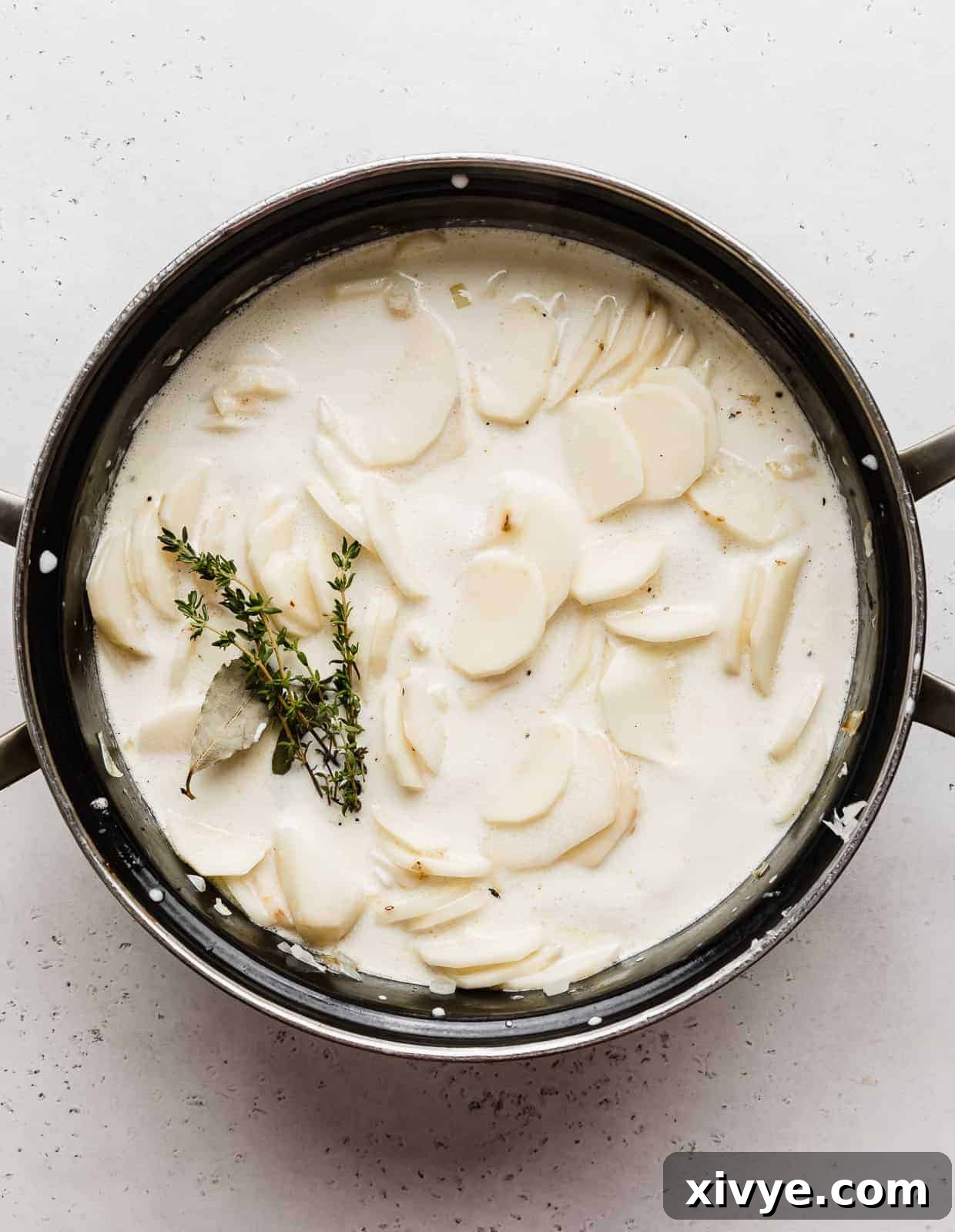Ultimate Gluten Free Scalloped Potatoes 5 A large black pot full of heavy cream, thinly sliced potatoes, sprigs of thyme, and bay leaves.