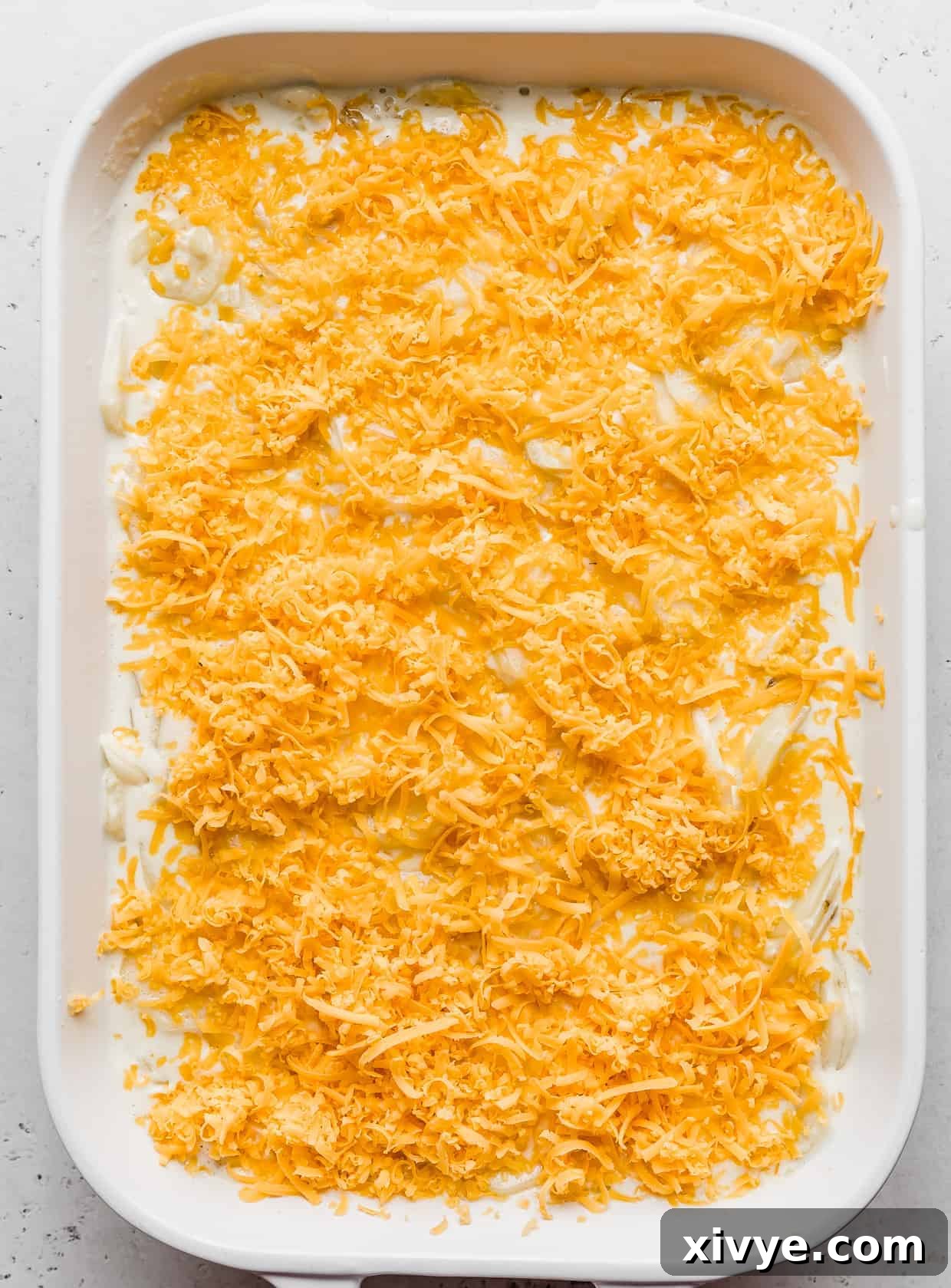 Ultimate Gluten Free Scalloped Potatoes 7 A white casserole dish topped with shredded cheddar cheese.