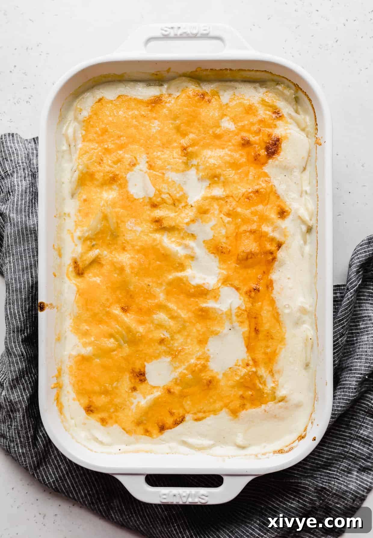 Ultimate Gluten Free Scalloped Potatoes 8 Melted cheddar cheese over thinly sliced potatoes in a creamy sauce against a gray background.