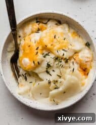 Ultimate Gluten Free Scalloped Potatoes 10 A Creamy Scalloped Potatoes Recipe in a white bowl topped with fresh thyme and cheese.