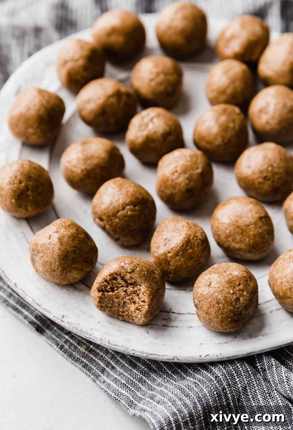 Snickerdoodle Energy Bites rolled into balls, sitting on a white plate with the closest one with a bite taken out of it.