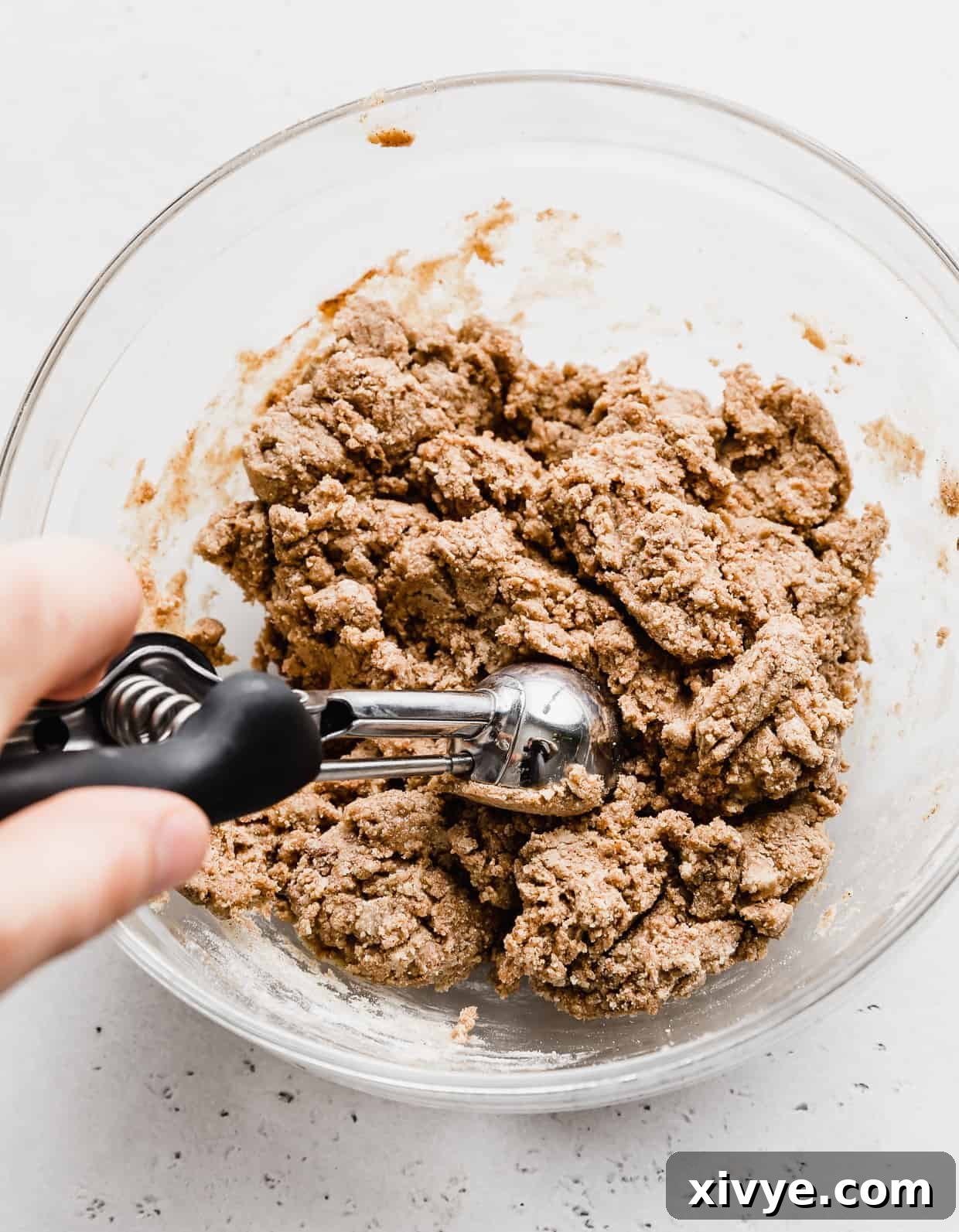 A small cookie scoop dipping into Snickerdoodle Energy Bites batter. 