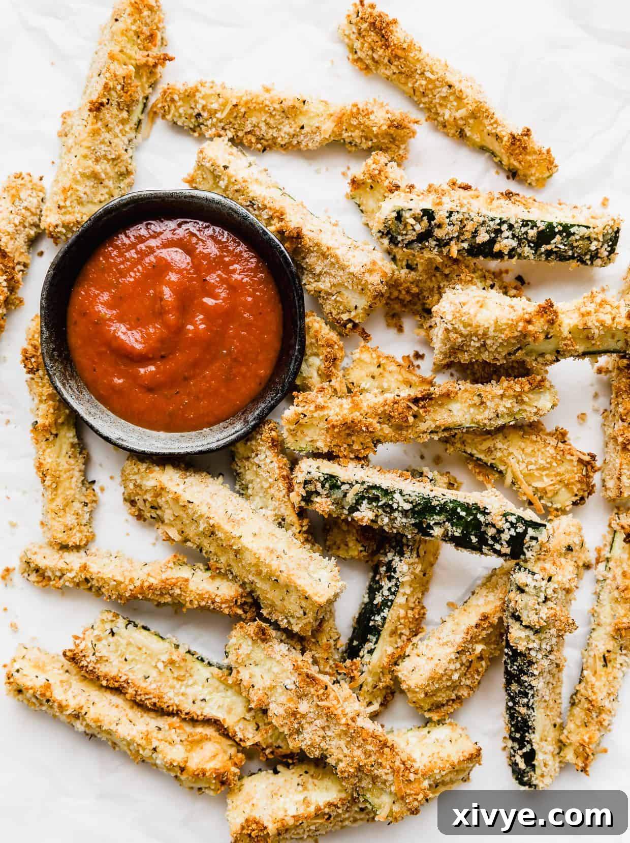 Zucchini fries on a white background with a small bowl of marinara sauce next to the fries.