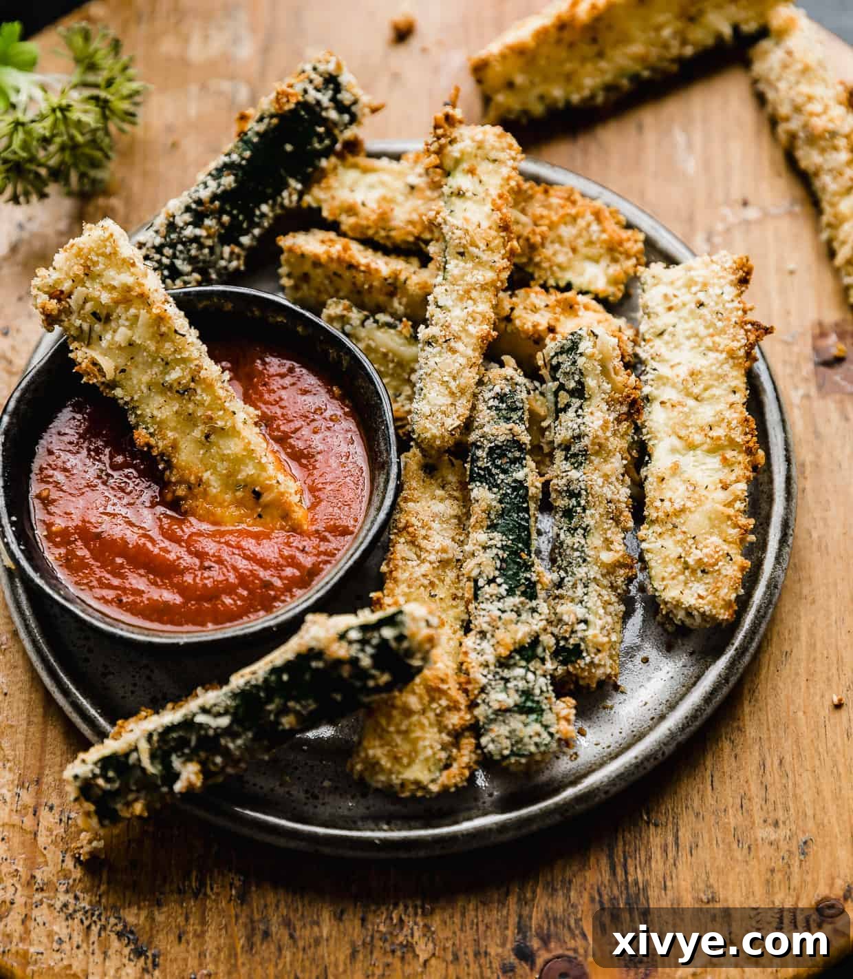 Zucchini fries on a black plate against a wooden background, with one zucchini fry dipped into pizza sauce.