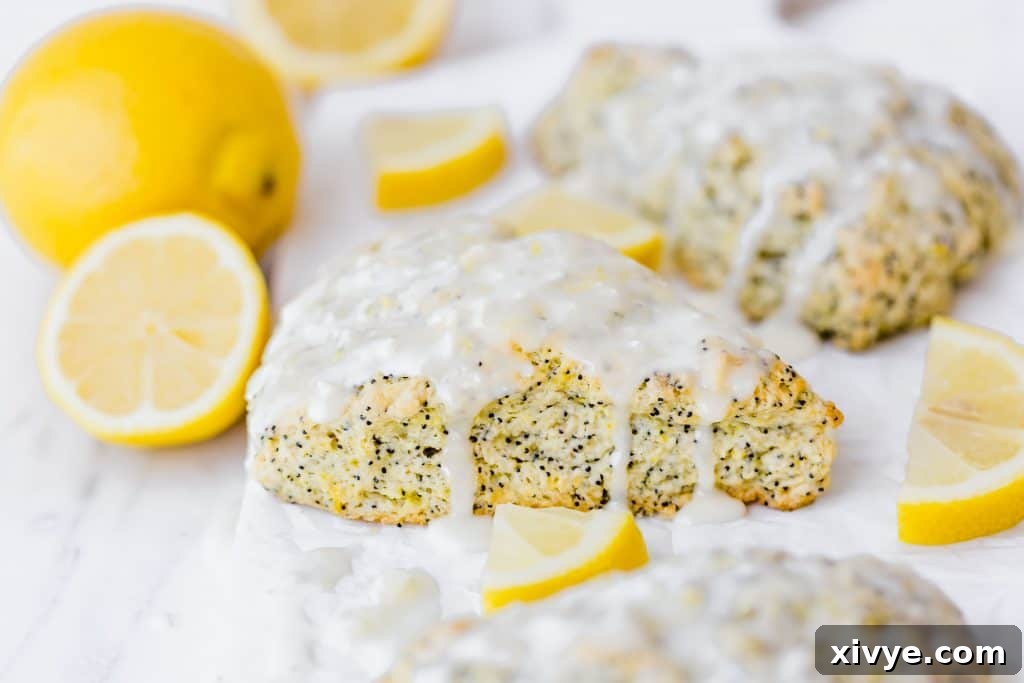 Sunshine Lemon Poppy Scones 7 Lemon poppy seed scone with a glaze drizzled overtop, surrounded by fresh lemons.