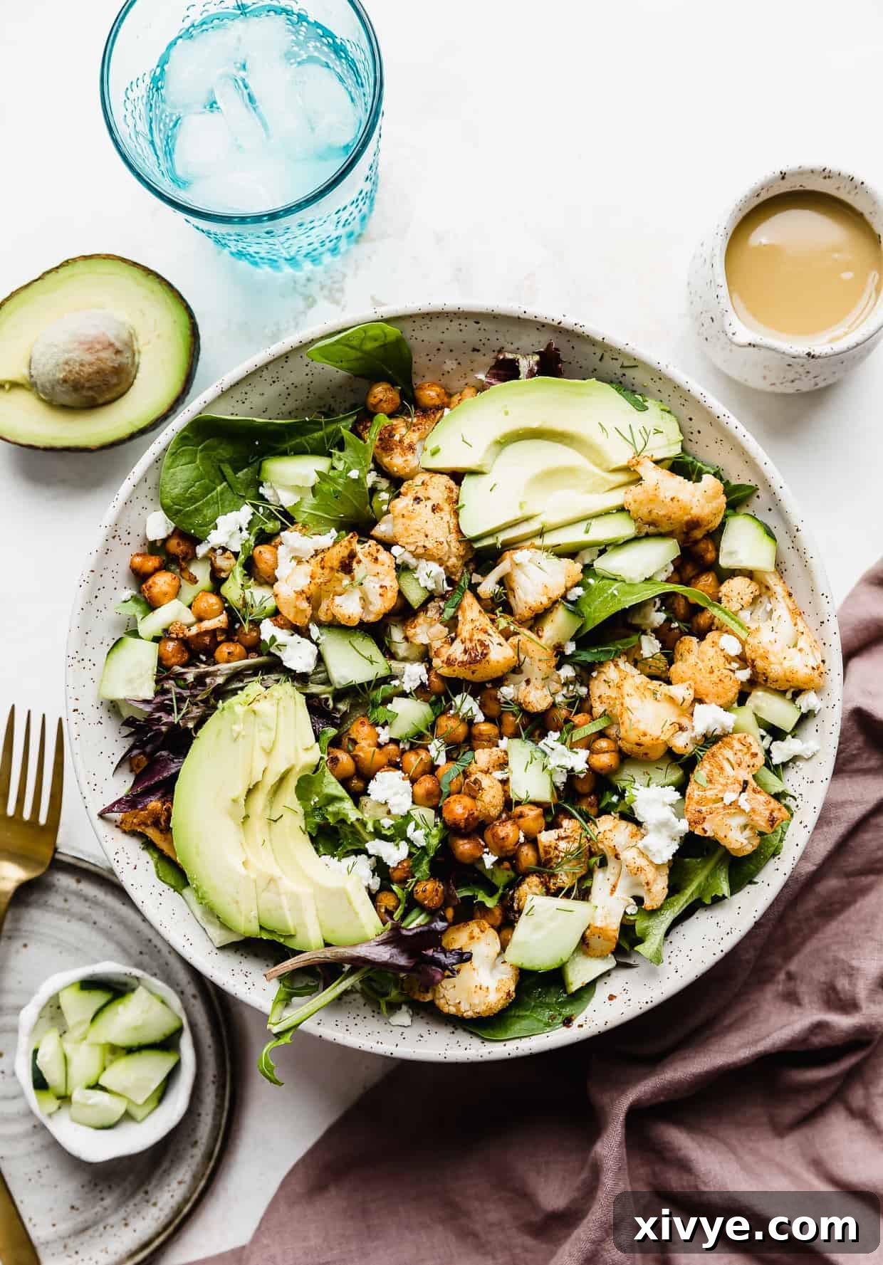 Roasted Cauliflower Salad in a large white bowl topped with sliced avocado and honey mustard dressing.