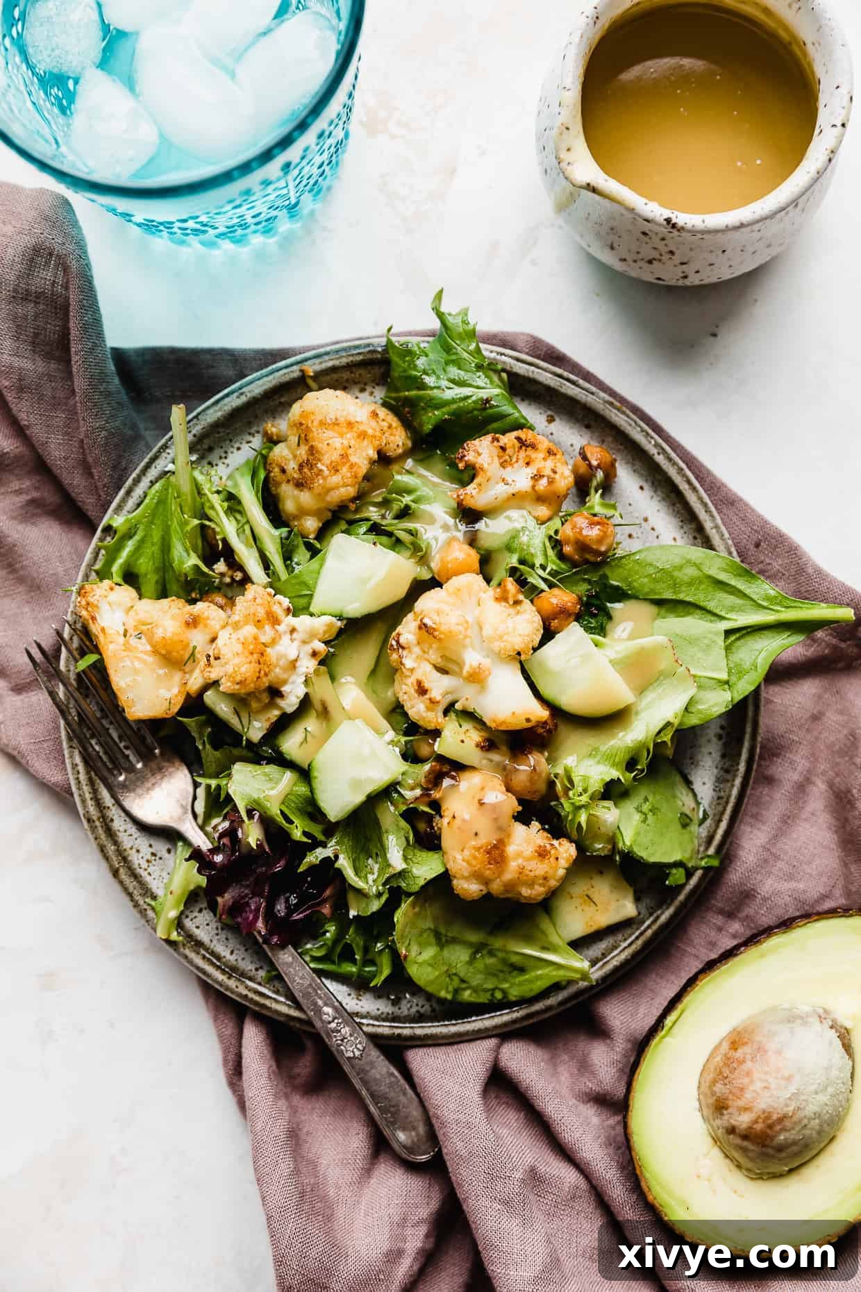 A gray plate with lettuce and roasted cauliflower and chickpeas, resting on a light purple linen napkin.