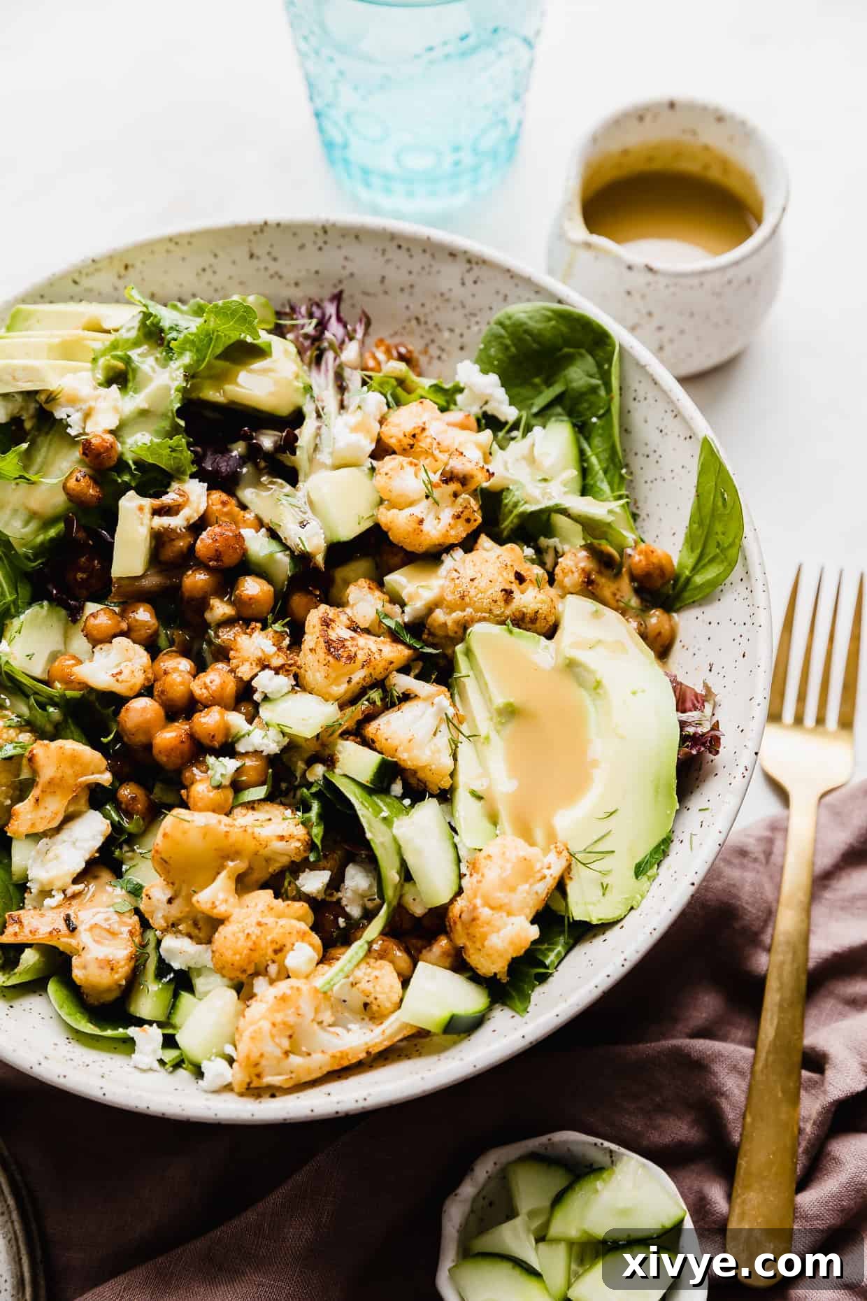 A salad in bowl topped with roasted cauliflower, sliced avocado, roasted chickpeas and a creamy yellow dressing.