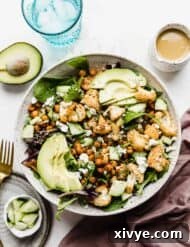 Roasted Cauliflower Salad in a large white bowl topped with sliced avocado and honey mustard dressing.