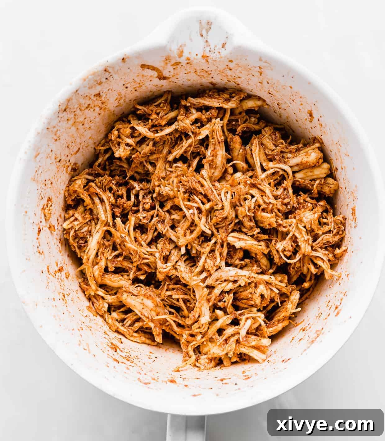 Golden Honey Lime Chicken Enchiladas 4 A white bowl full of shredded chicken covered in a red and orange colored marinade.