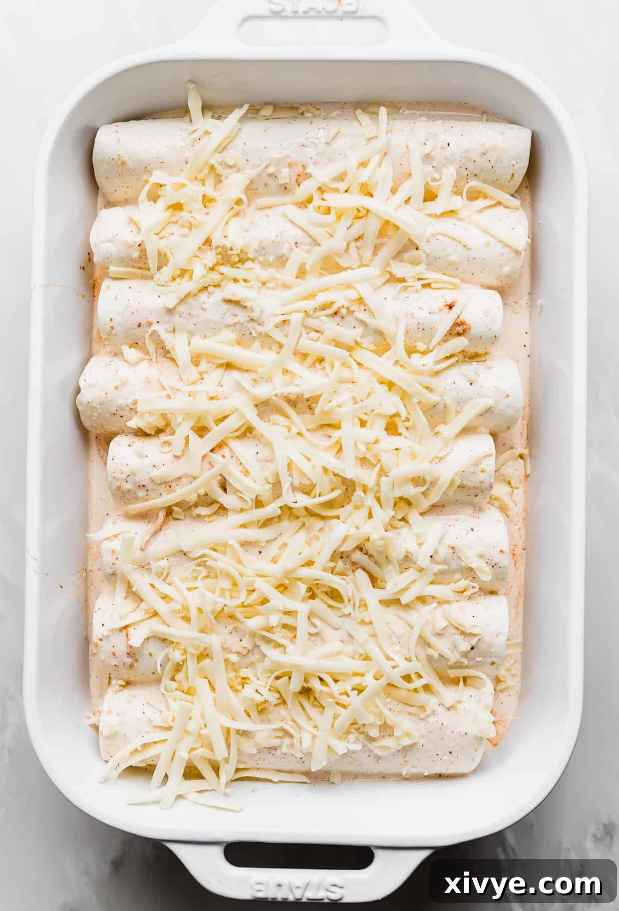 Golden Honey Lime Chicken Enchiladas 6 White shredded cheese overtop rolled up flour tortilla enchiladas in a casserole dish.