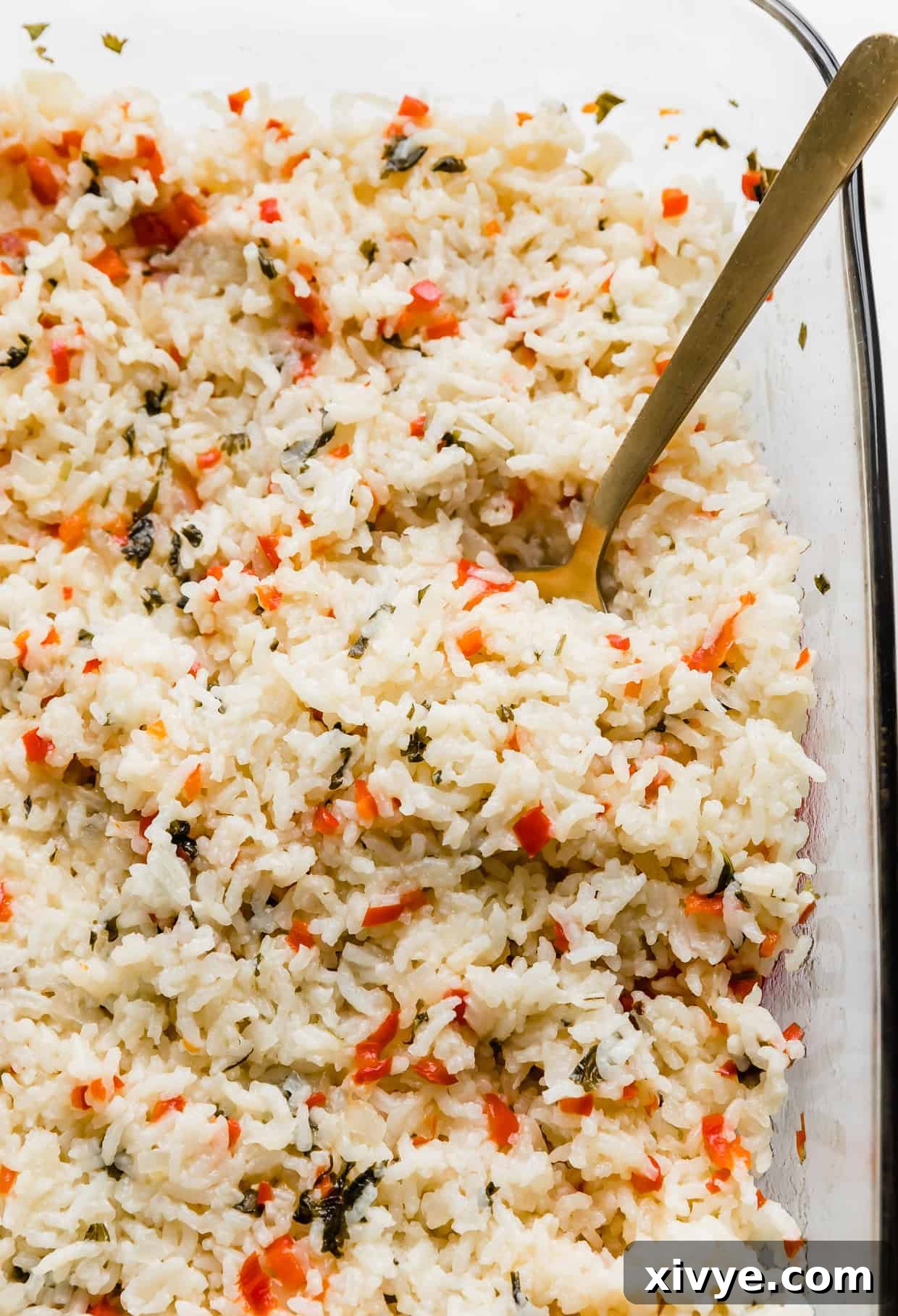 Sweet Bell Pepper Pilaf 2 A spoon in a baking dish full of Sweet Pepper Rice that is studded with diced red peppers and chopped cilantro.