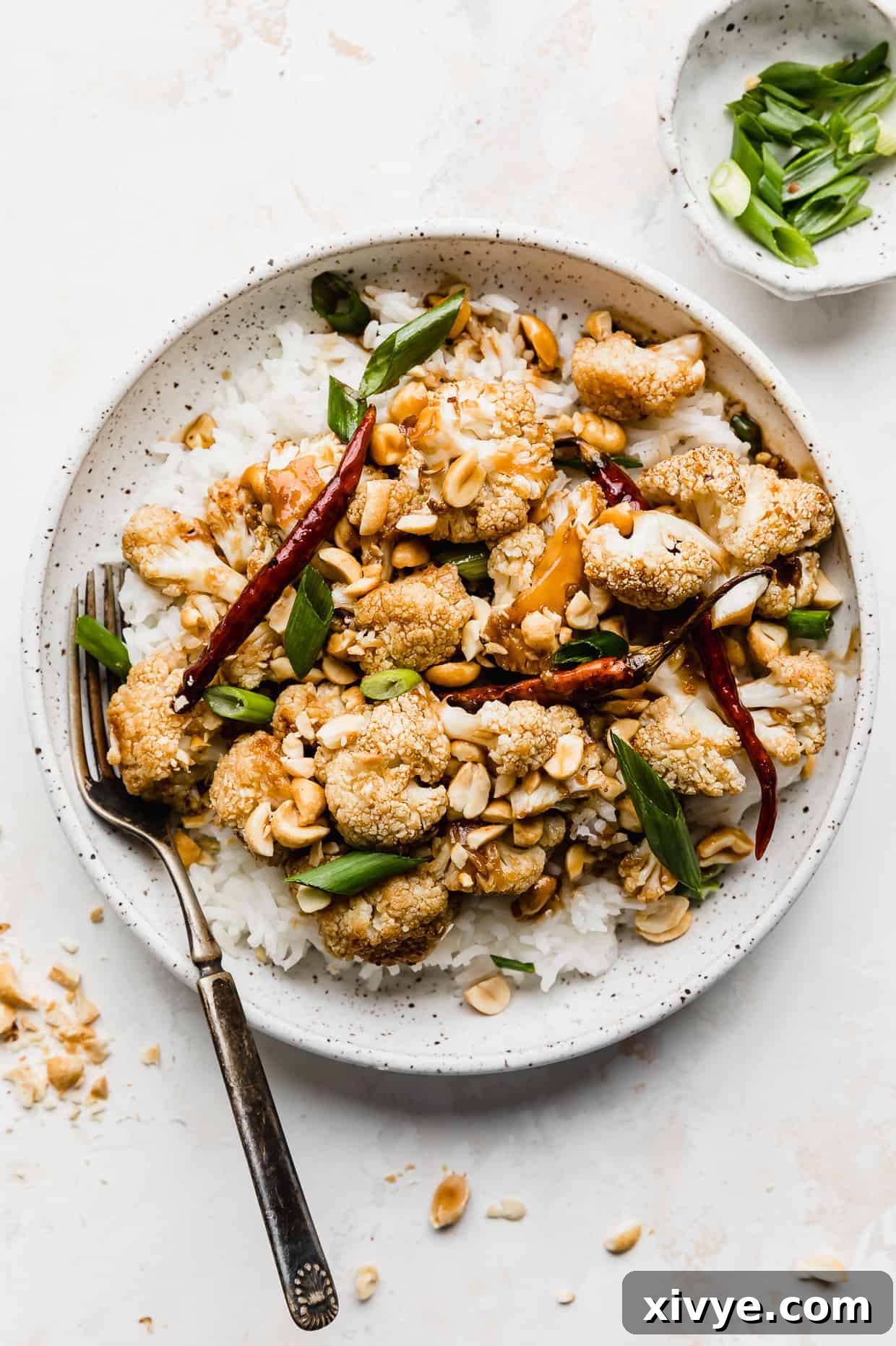 A white plate full of Kung Pao Cauliflower against a white background.