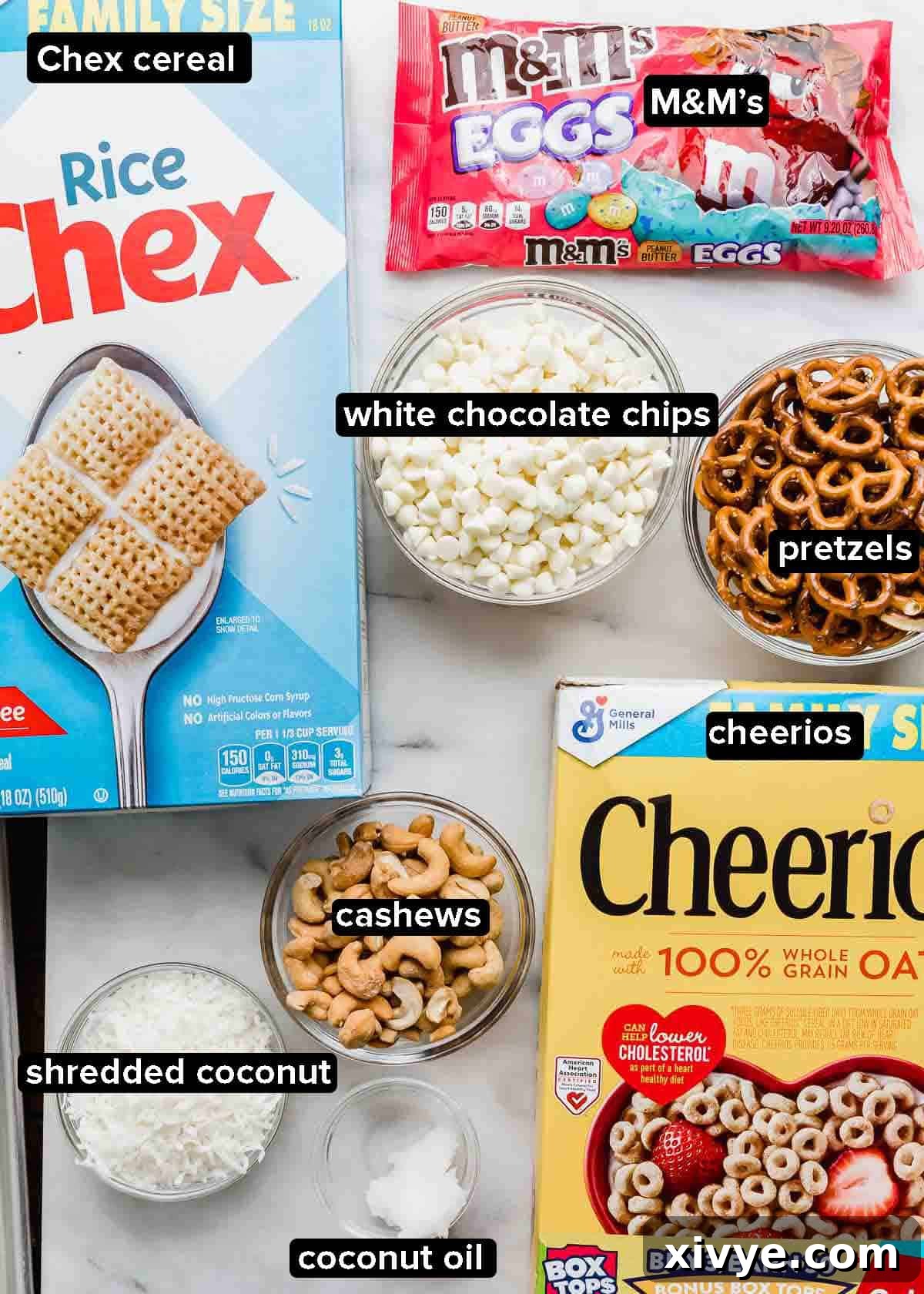 Easter Bunny Crunch Mix 3 Bunny Bait ingredients laid out on a white background: Cheerios, Chex cereal, M&M's, white chocolate chips, pretzels, nuts, and coconut, ready for mixing.