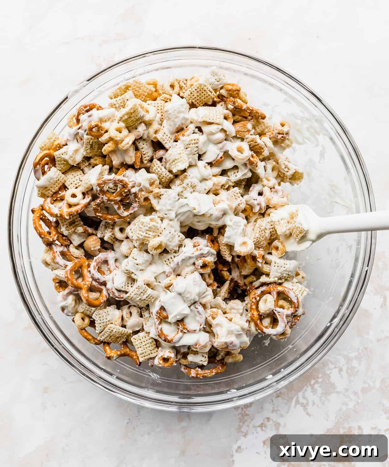 Easter Bunny Crunch Mix 4 White chocolate being stirred into a glass bowl with pretzels, cashews, and cheerios, ensuring an even coating.