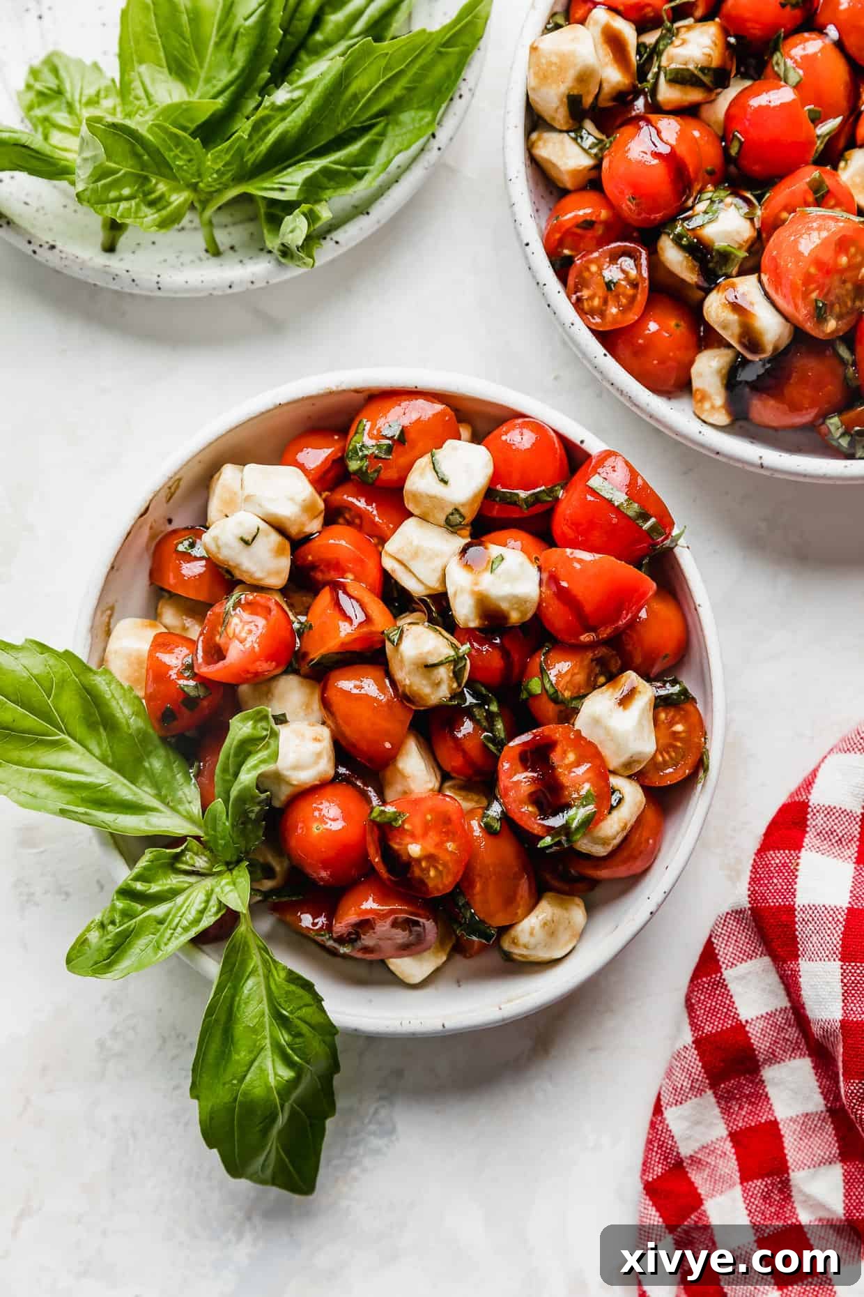 Vibrant Cherry Tomato Caprese Salad 2 A white bowl full of sliced cherry tomatoes, mozzarella balls, and fresh basil drizzled with balsamic glaze.