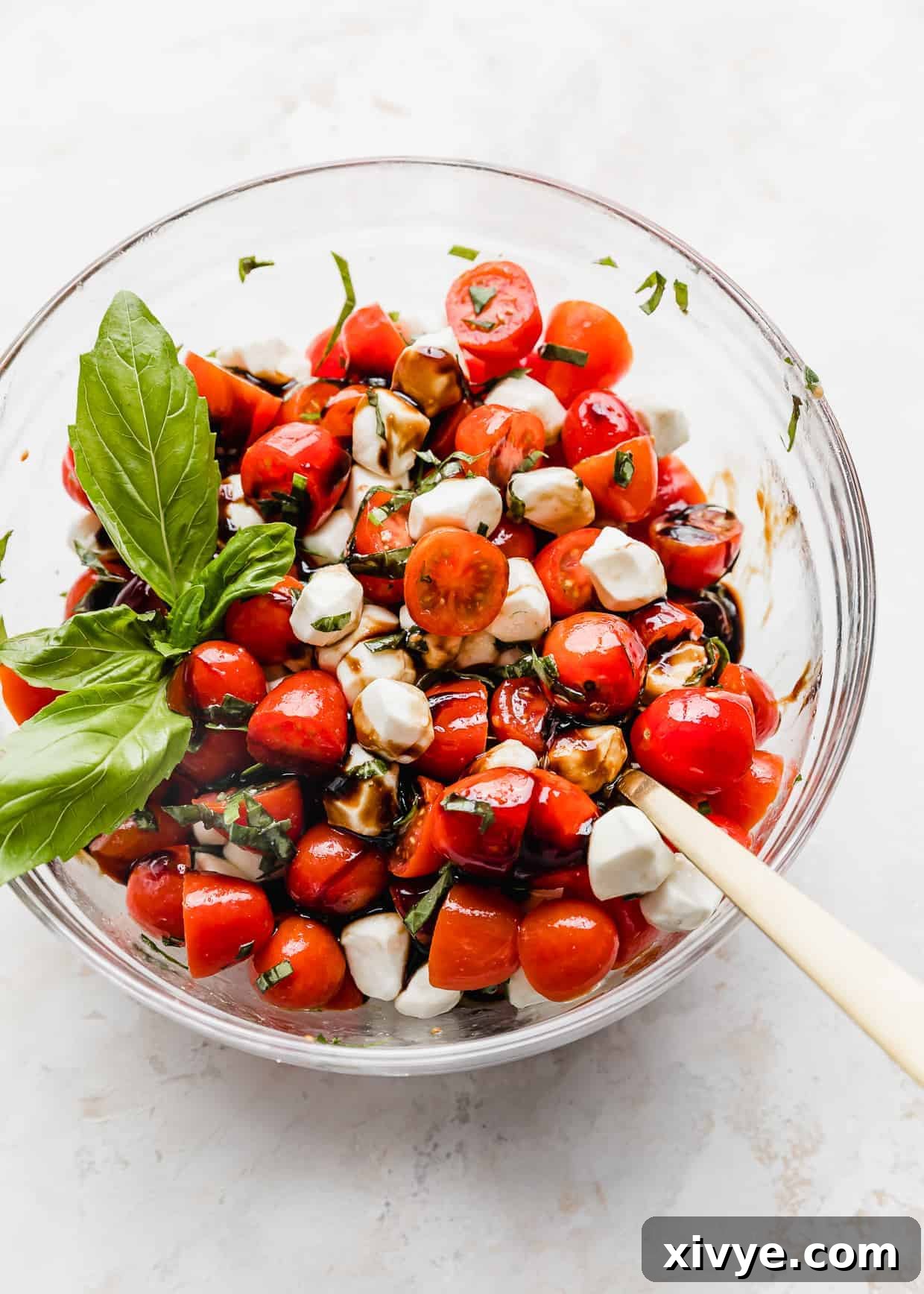 Vibrant Cherry Tomato Caprese Salad 3 A glass bowl full of red grape or cherry tomatoes with mozzarella balls, chopped basil, and balsamic glaze.