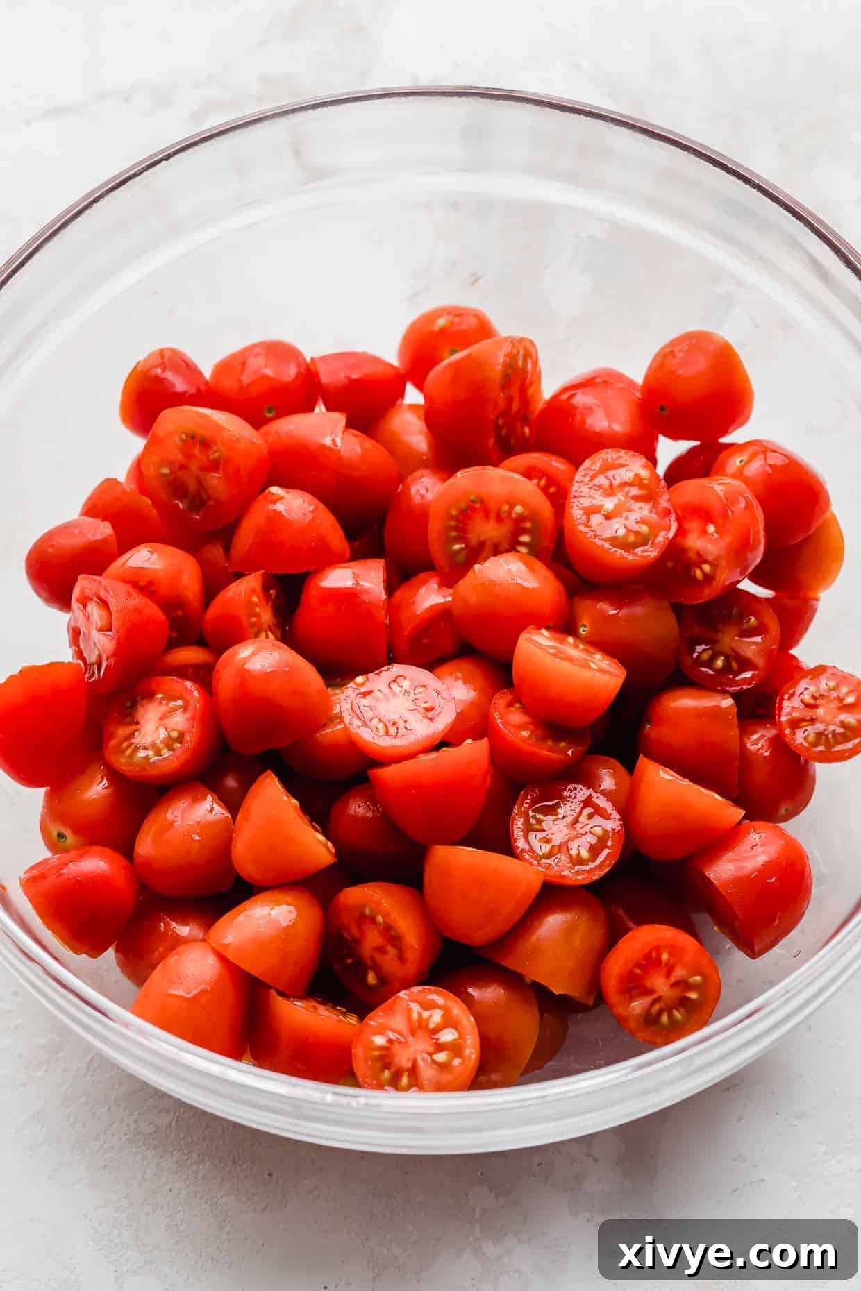 Vibrant Cherry Tomato Caprese Salad 4 Red Cherry tomatoes cut in half, in a glass bowl.