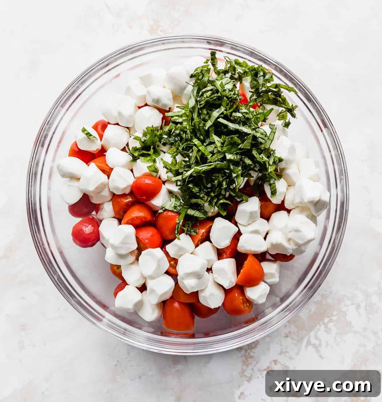 Vibrant Cherry Tomato Caprese Salad 5 A glass bowl with sliced cherry tomatoes, chopped basil, and mozzarella balls.
