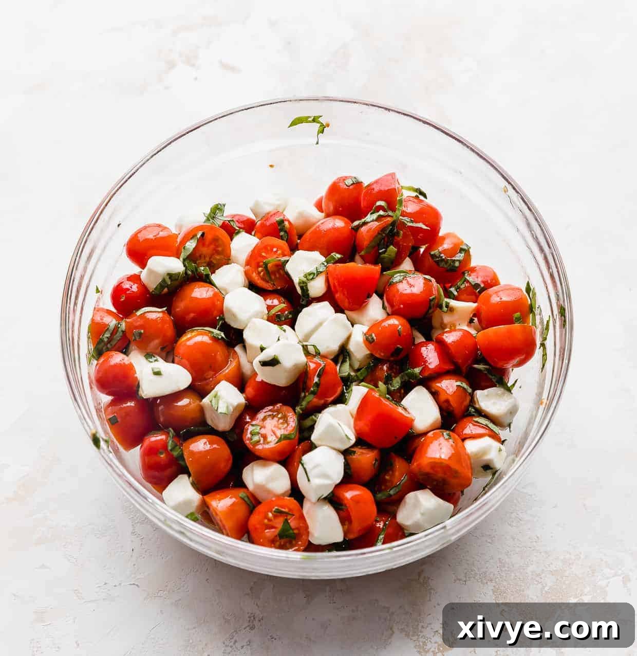 Vibrant Cherry Tomato Caprese Salad 6 A glass bowl full of red grape tomatoes tossed with mozzarella balls and chopped basil.