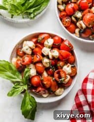 A white bowl full of sliced cherry tomatoes, mozzarella balls, and fresh basil drizzled with balsamic glaze.