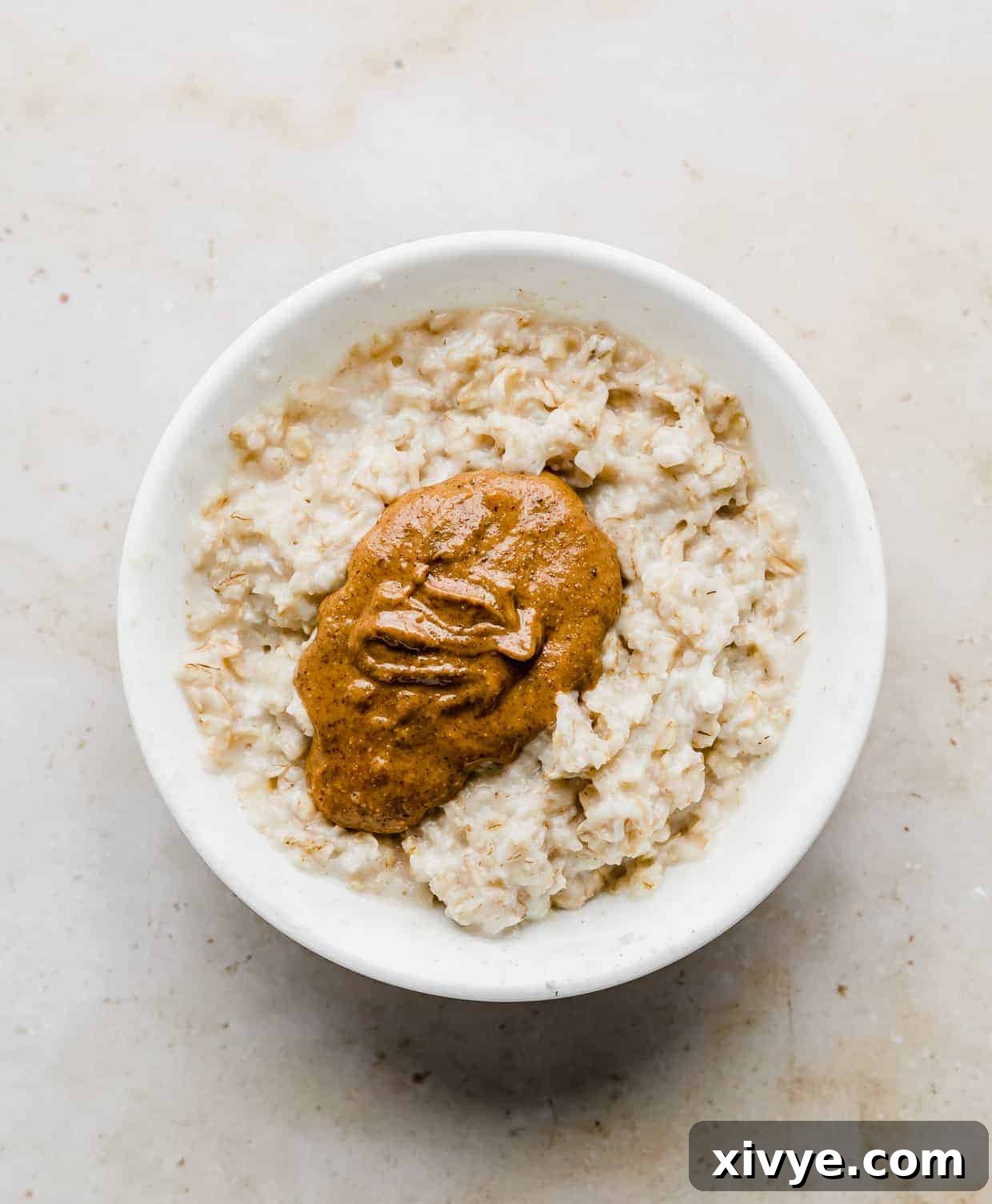 A white bowl with cooked oatmeal and a dollop of almond butter in it.