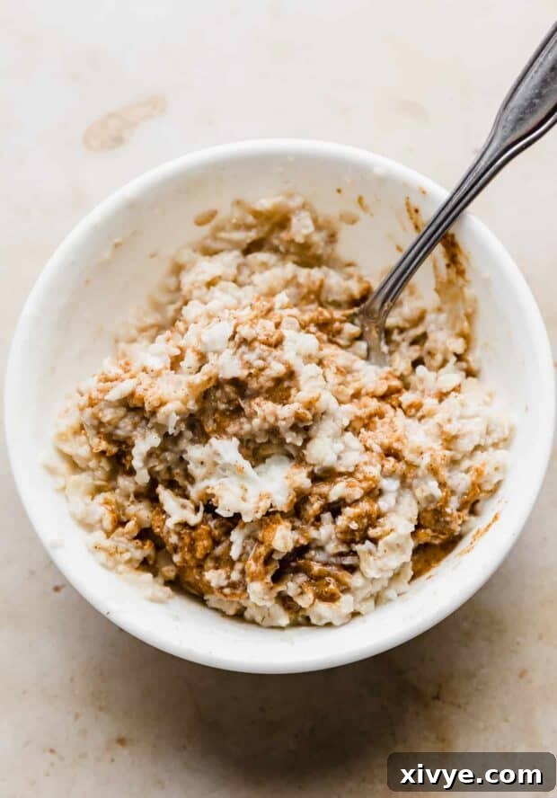 Almond butter and cooked oatmeal being stirred in a white bowl.
