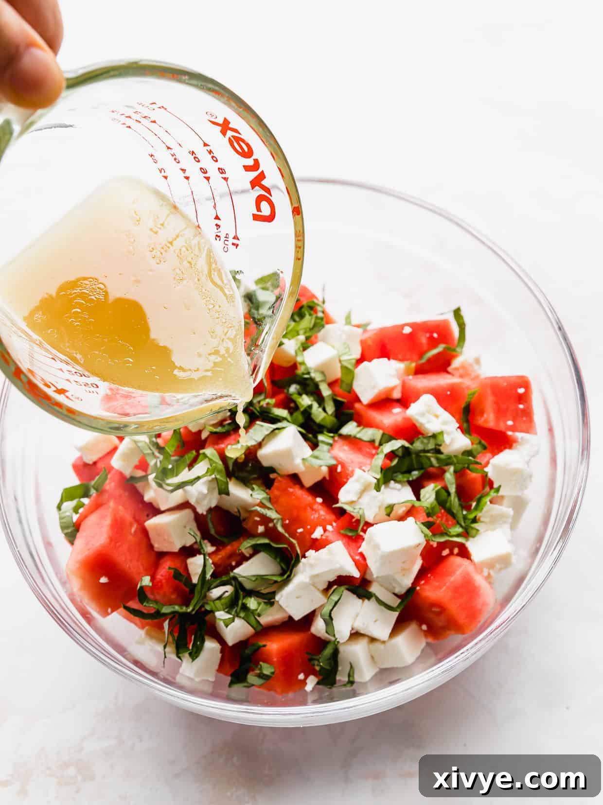 Sweet and Savory Watermelon Feta Basil Salad 4 A dressing being poured over a Watermelon Feta Basil Salad in a glass bowl.