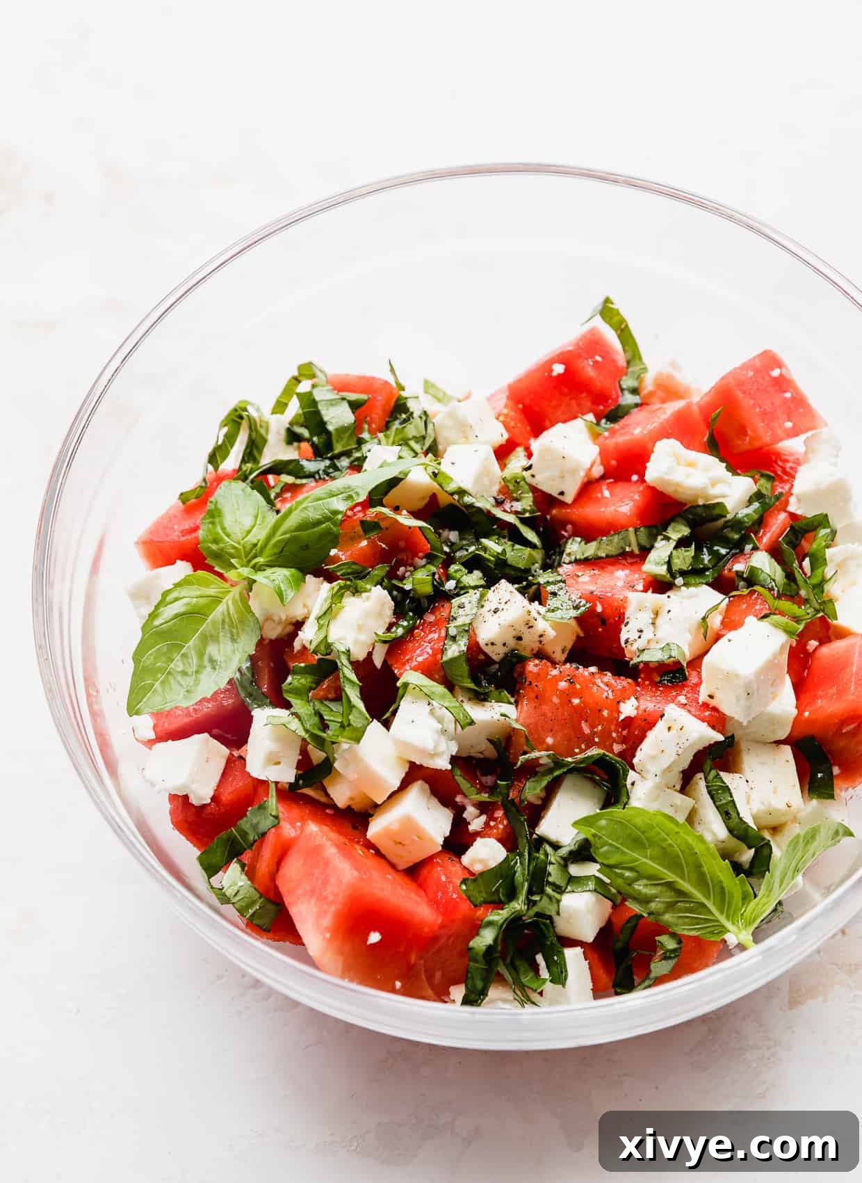 Sweet and Savory Watermelon Feta Basil Salad 5 A Watermelon Feta Basil Salad in a glass bowl against a white background.