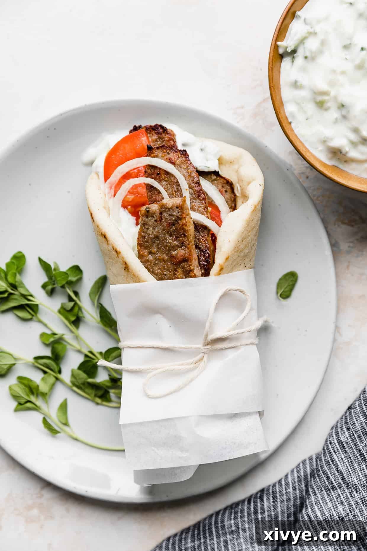 Tender Lamb Gyros 75 A lamb gyro wrapped in white parchment paper on a white plate.