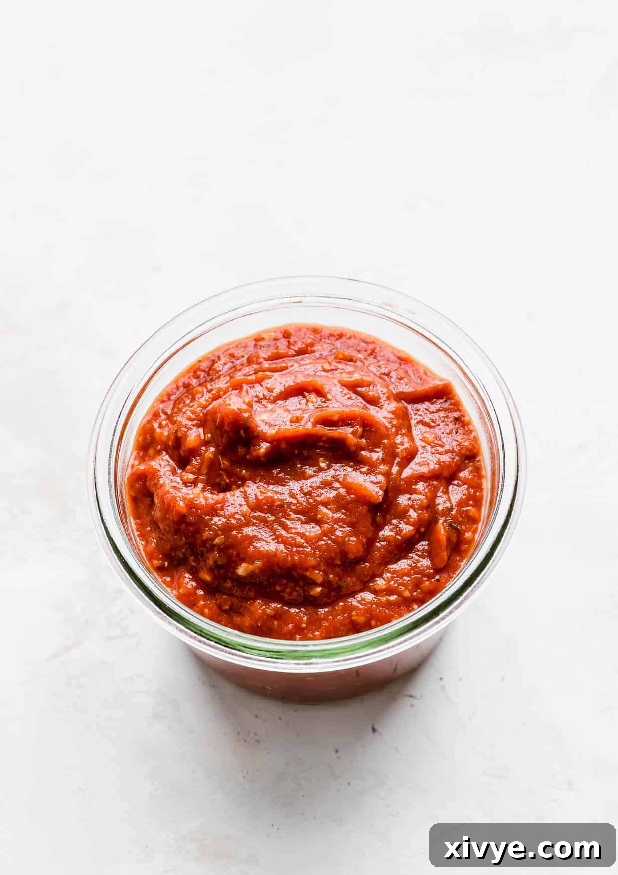 A jar of homemade pizza sauce made with tomato paste, against a clean white background, showcasing its rich, thick consistency.