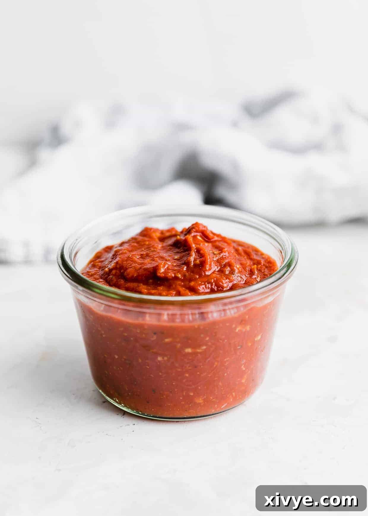 A glass jar filled with finished Pizza Sauce made from Tomato Paste, set against a pristine white background, ready to be stored or used.