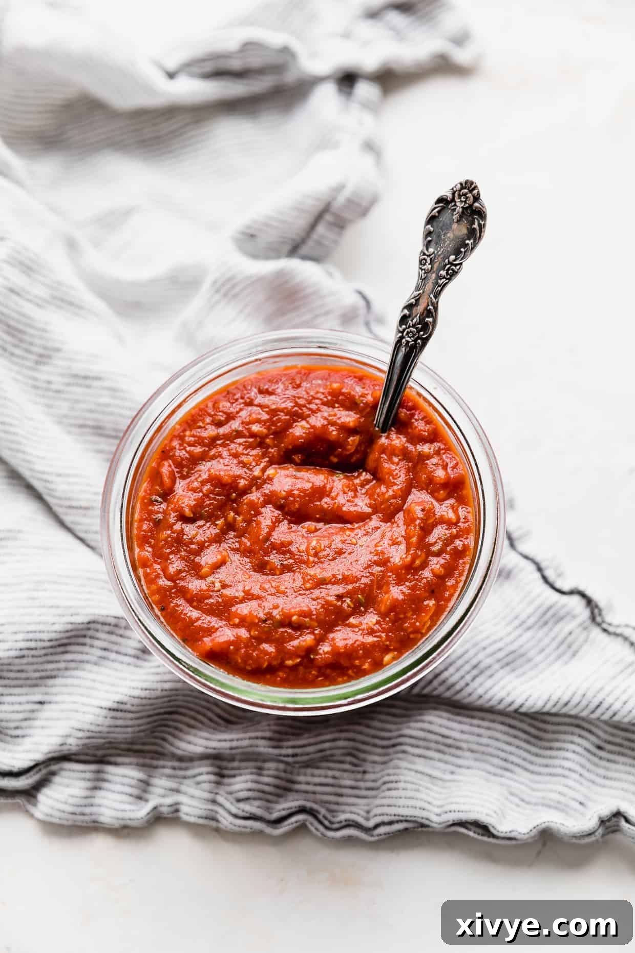 An overhead shot of a glass jar filled with homemade Pizza Sauce made from Tomato Paste, placed on a white surface.