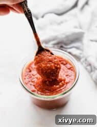 A spoon scooping up homemade pizza sauce from a glass jar.