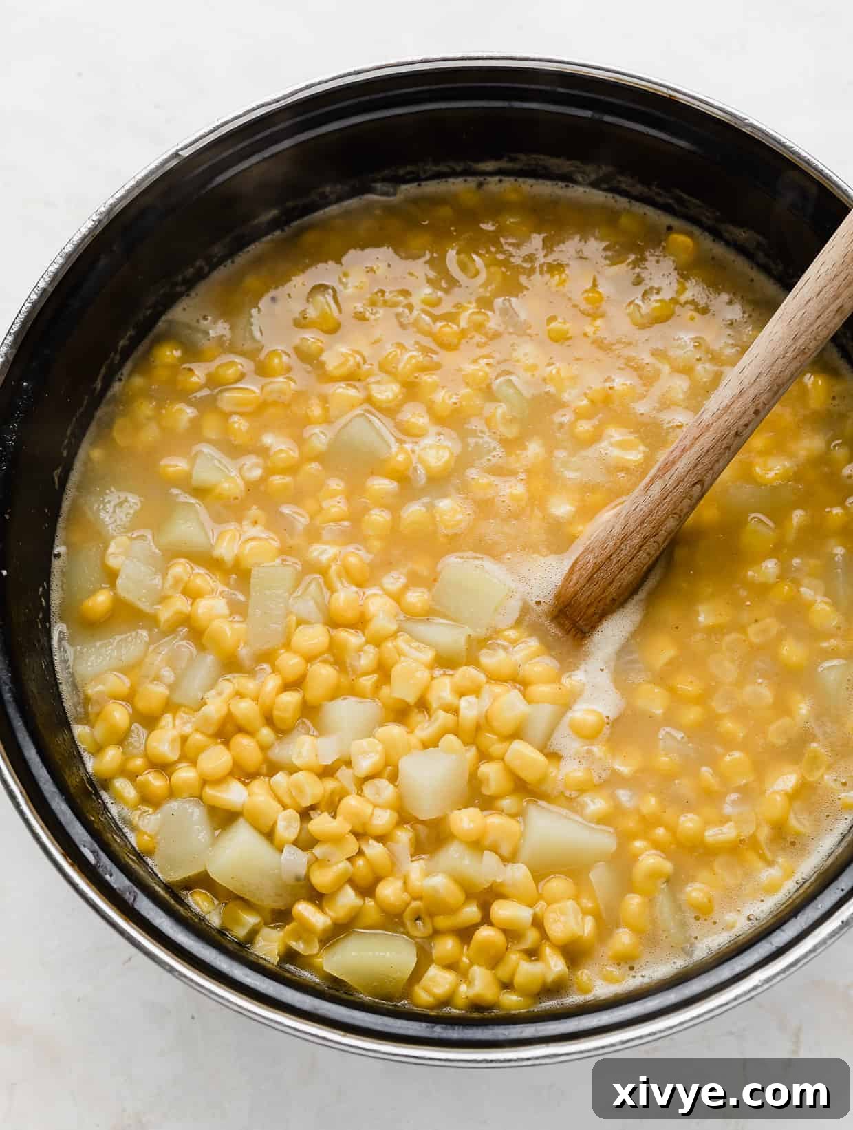 Creamy Ham and Sweet Corn Chowder 8 A wooden spoon stirring a large pot full of cooked corn and diced potatoes.