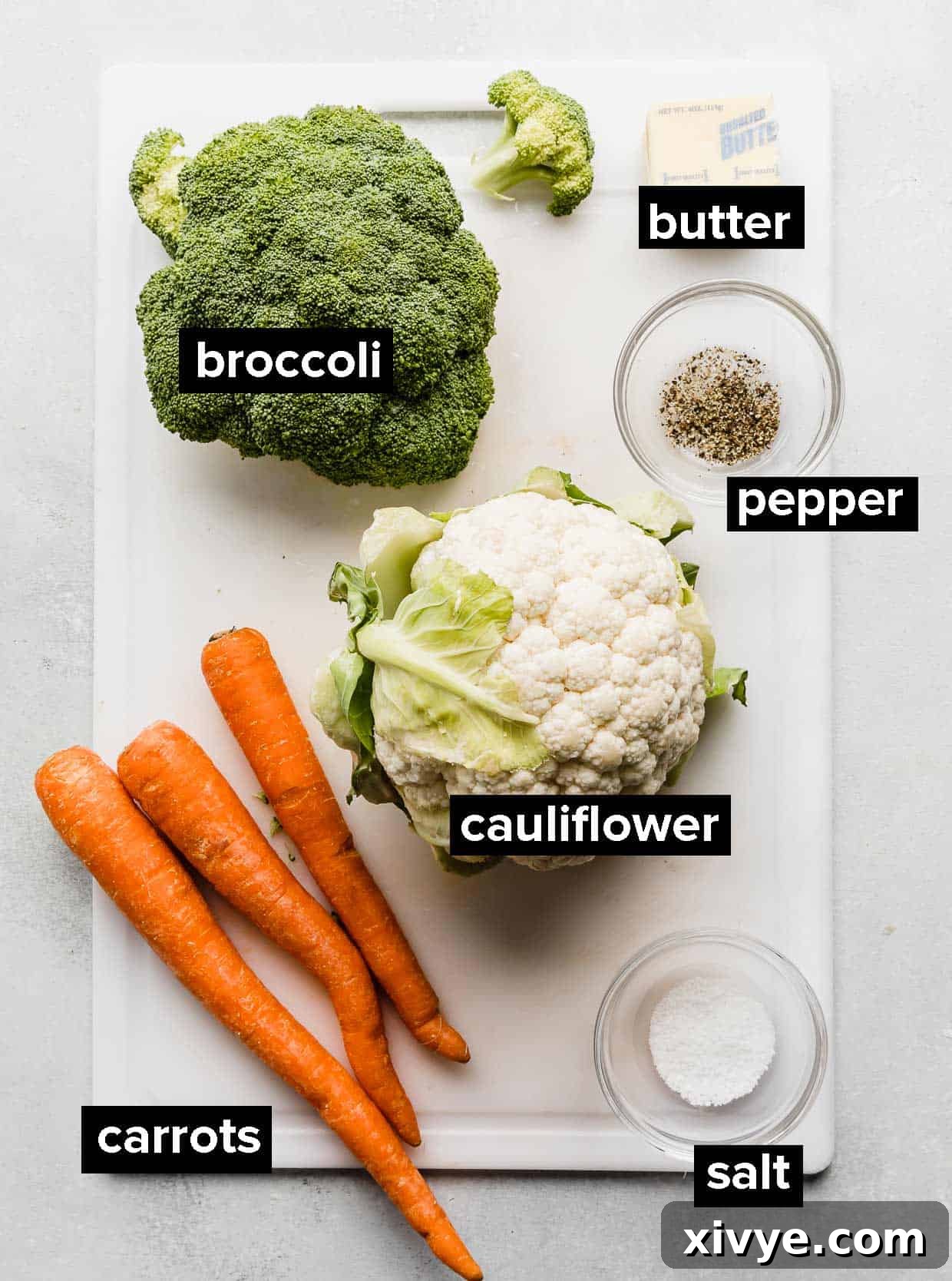 Ingredients used to make buttered vegetables on a white cutting board. 