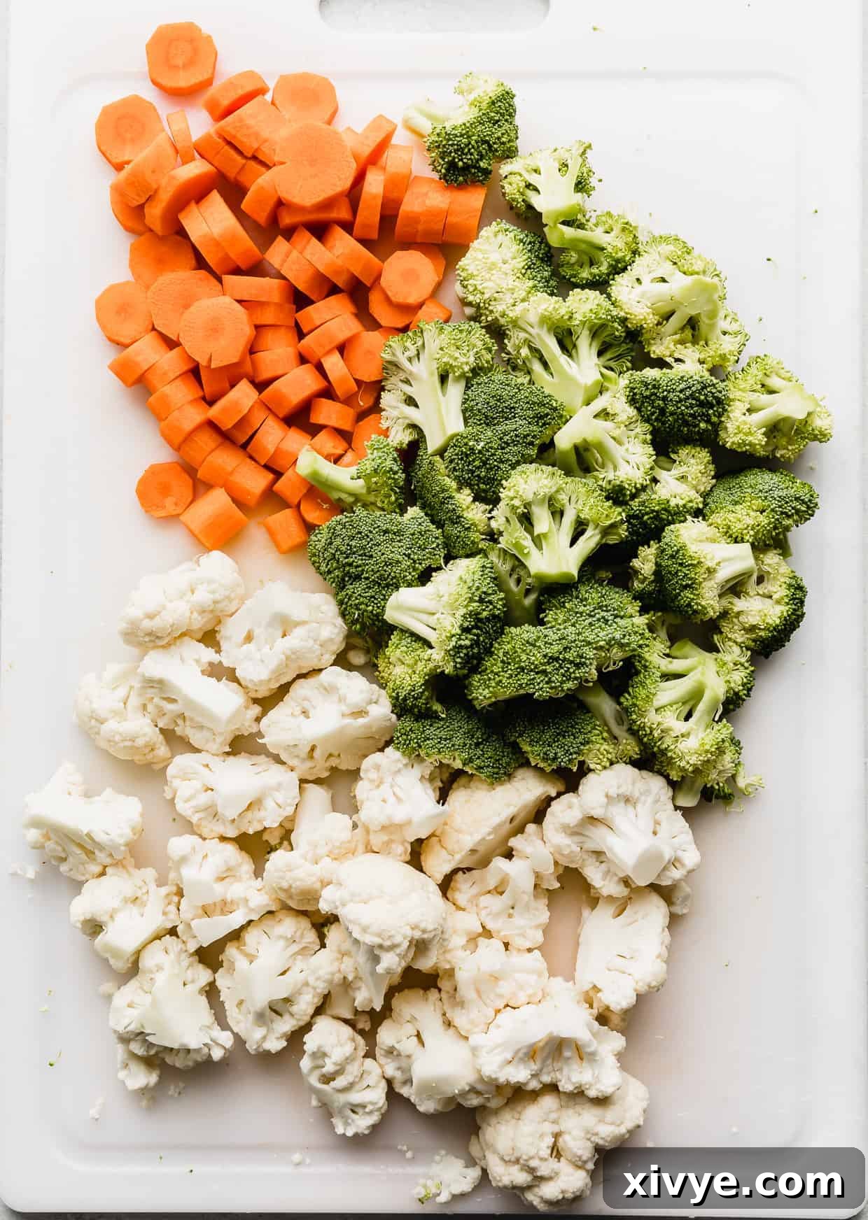 Chopped cauliflower, broccoli, and carrots on a white cutting board.
