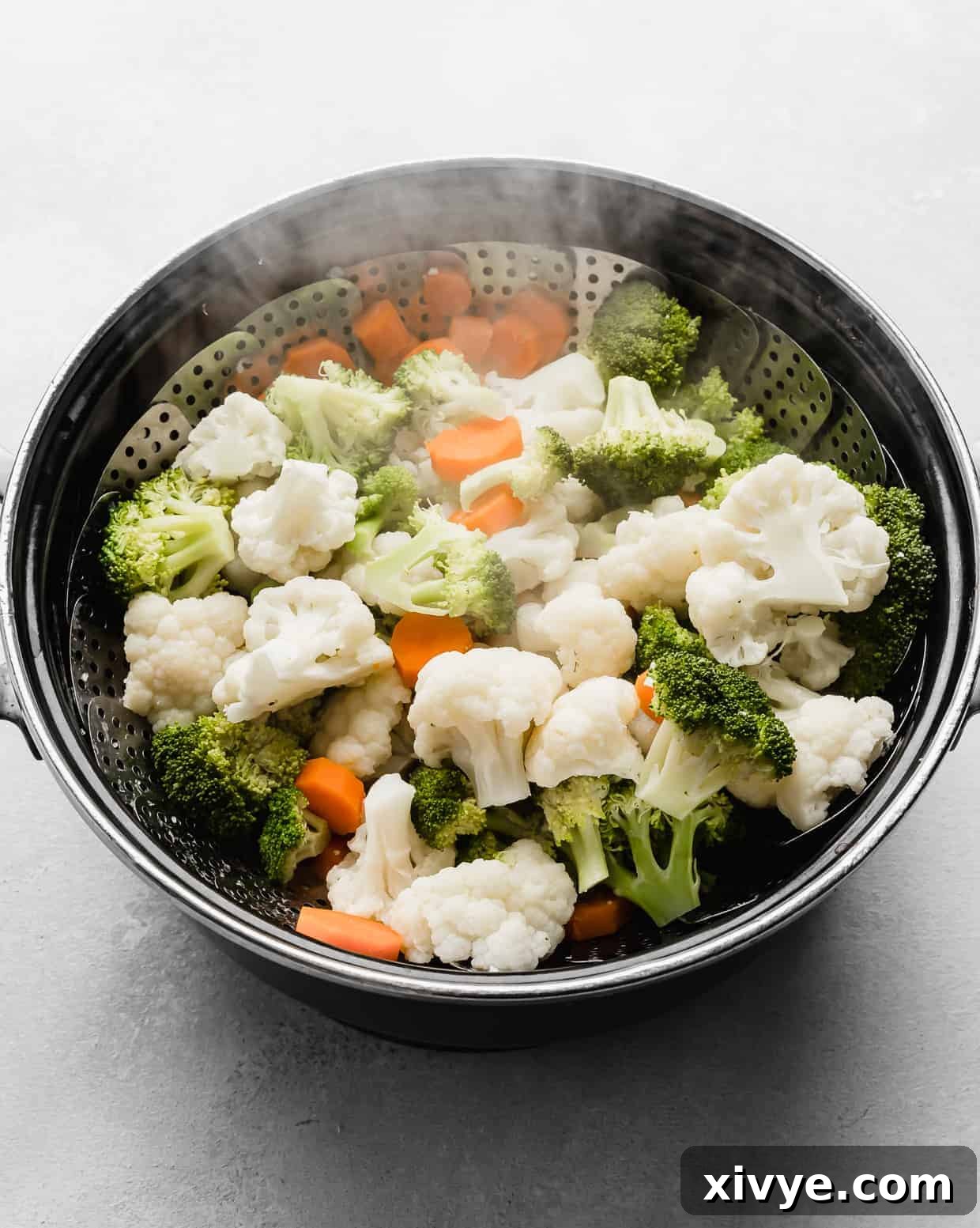 Freshly steamed broccoli, cauliflower, and carrots in a black pot.