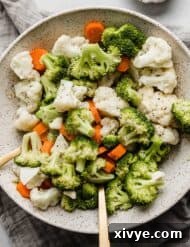 A bowl full of steamed and buttered broccoli, cauliflower, and carrots.