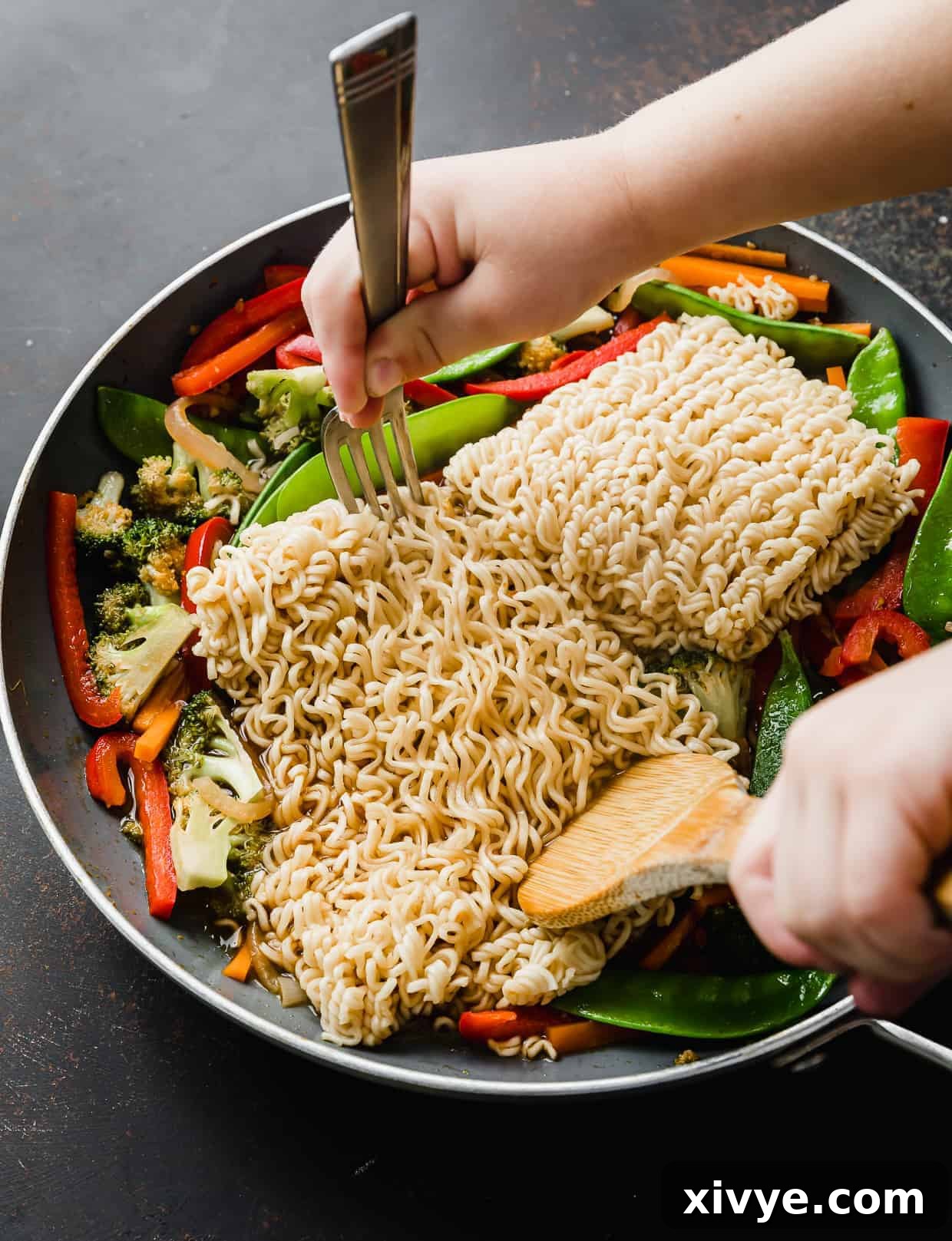 Cooked ramen noodles in a skillet being separated by a wooden spoon and fork.
