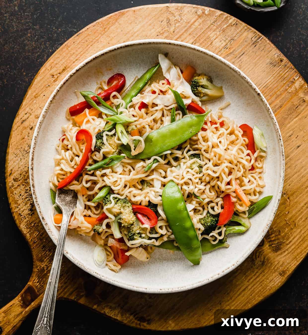 A bowl of Ramen with Vegetables on a wooden circle cutting board. 