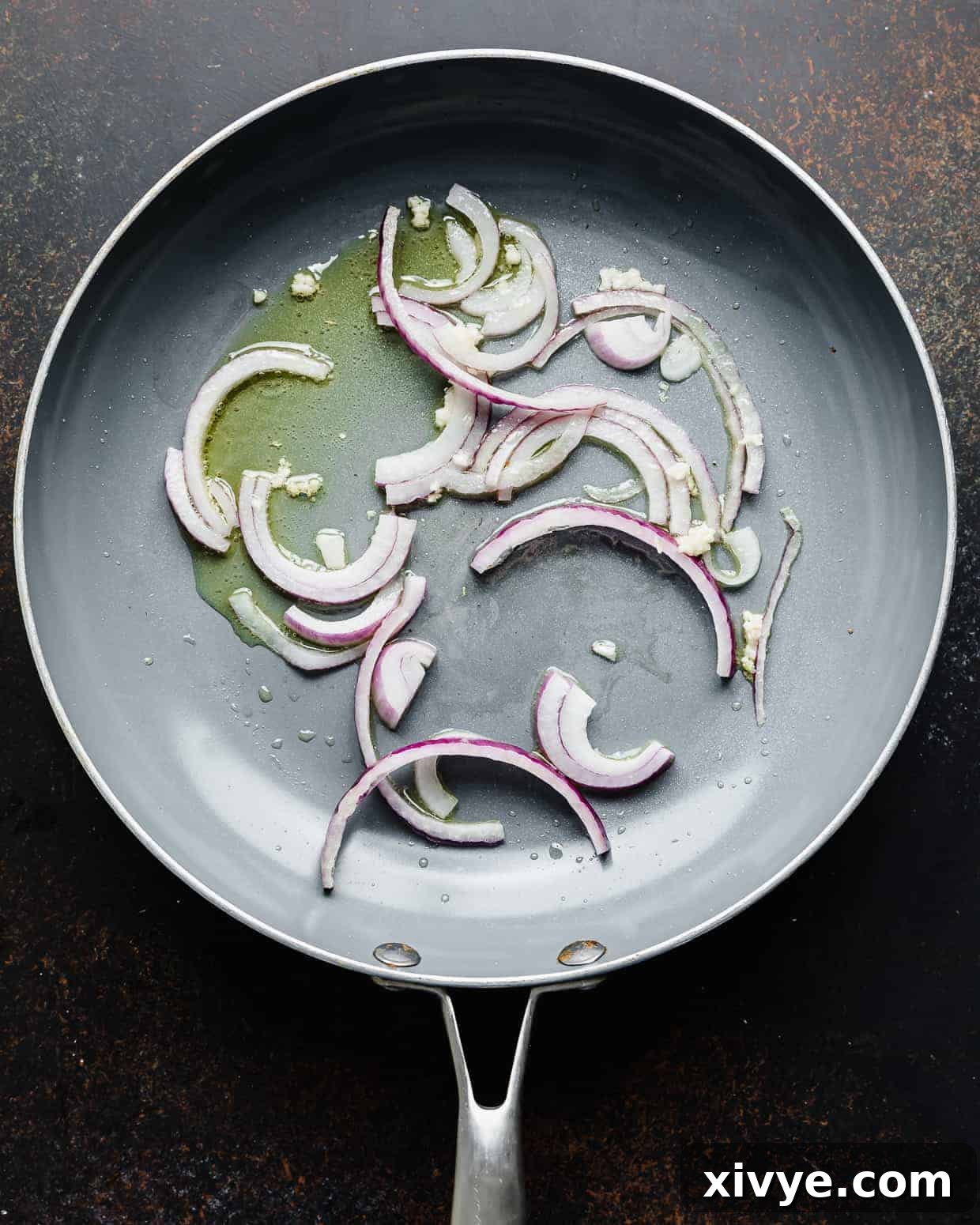 A gray skillet with sliced red onions and minced garlic in it. 