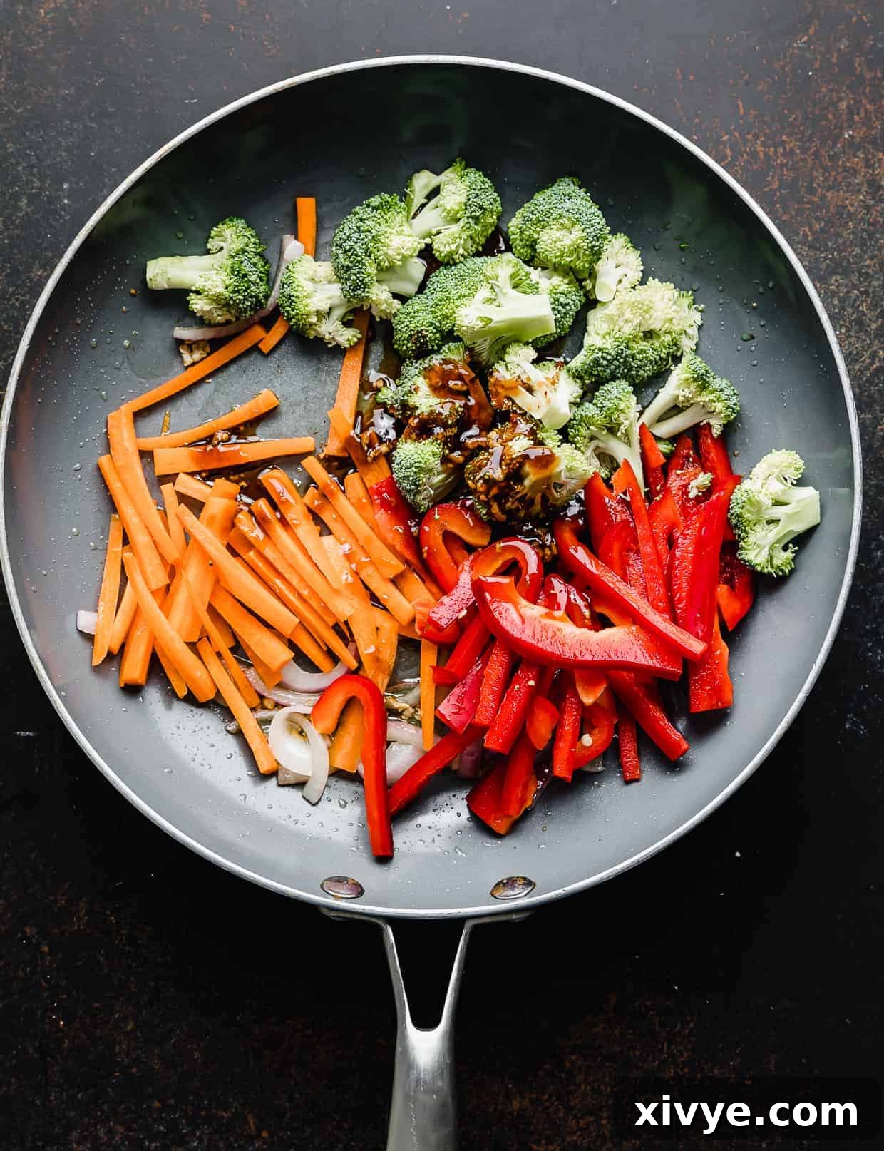A skillet with red peppers, broccoli, carrots, and a brown sauce in it.