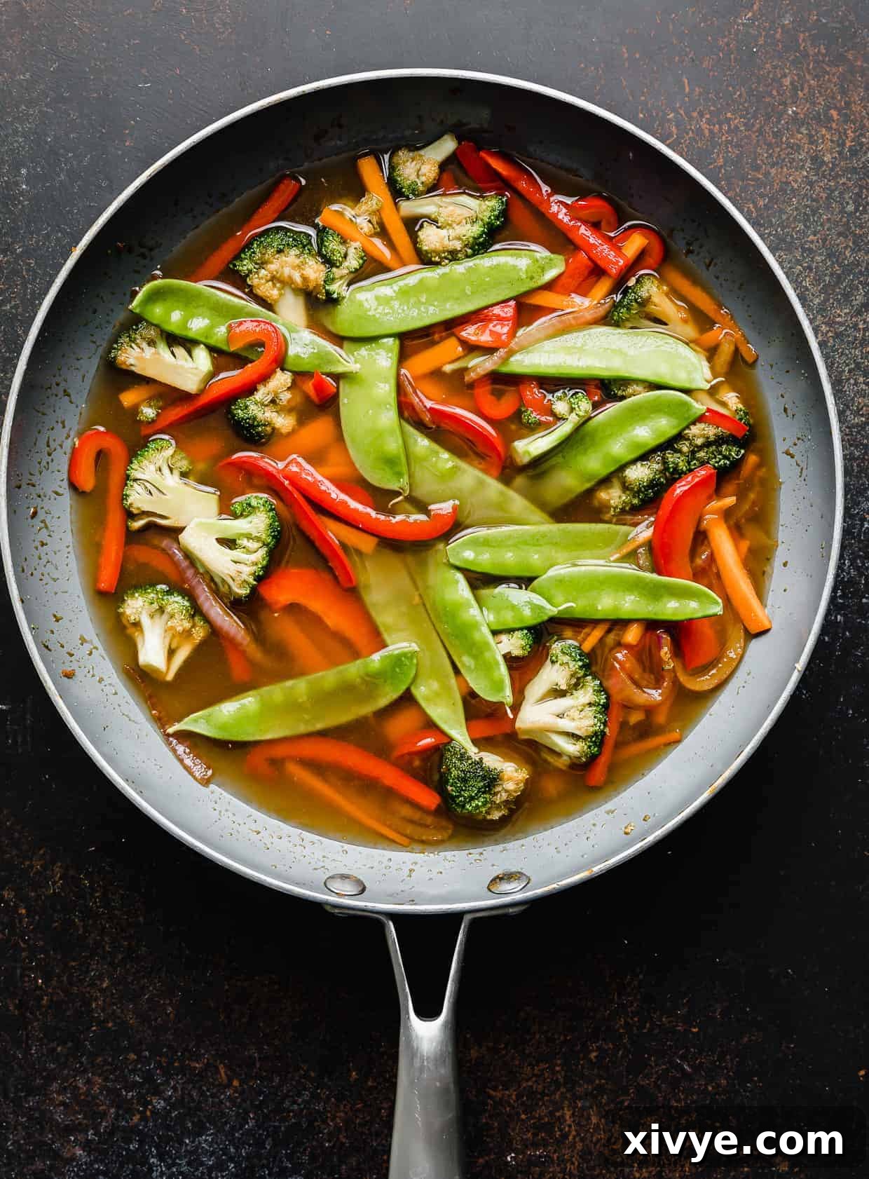 Snow peas and water added to a skillet with vegetables.