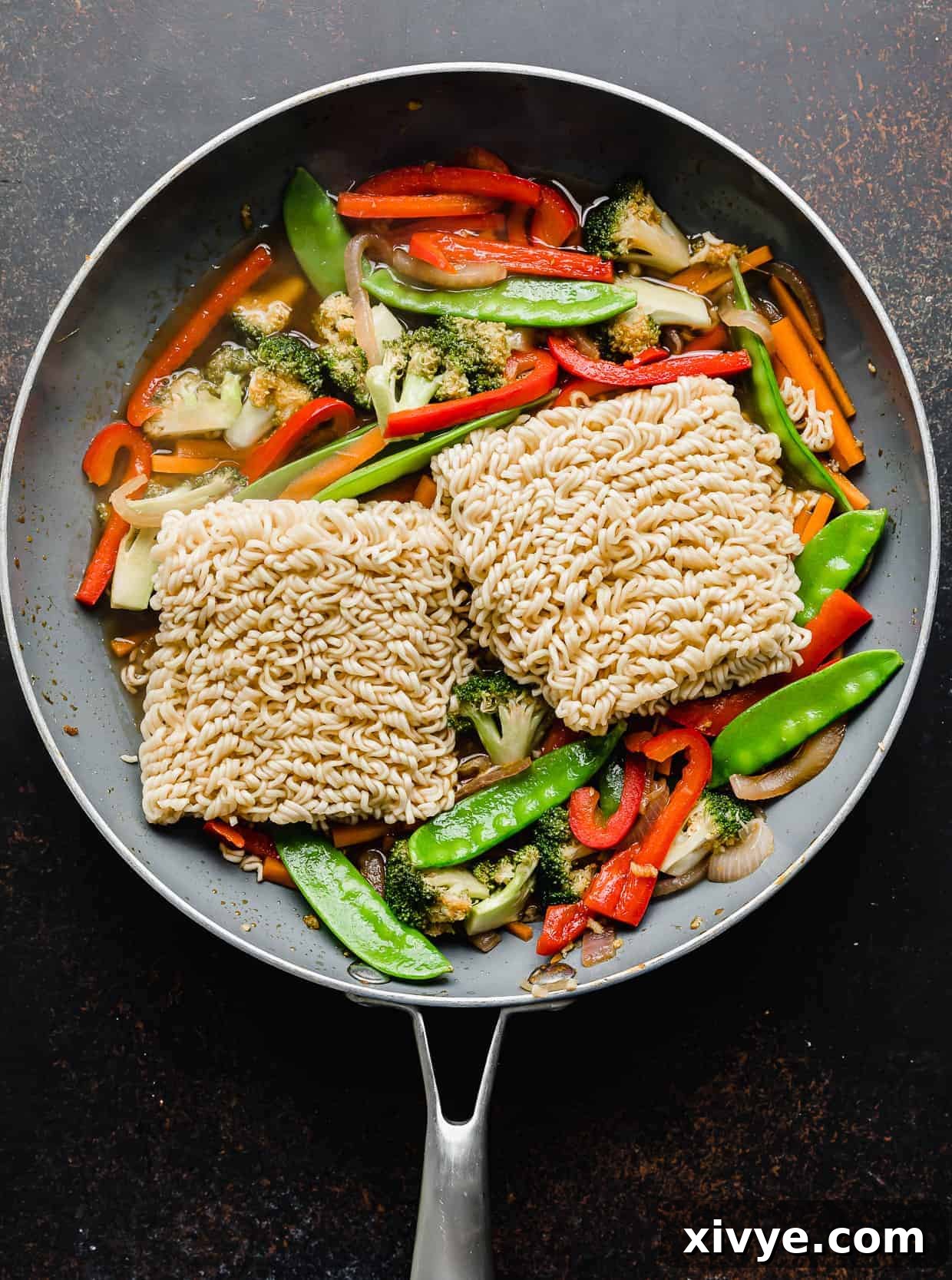 Two ramen noodles bundles in a skillet overtop sliced vegetables.