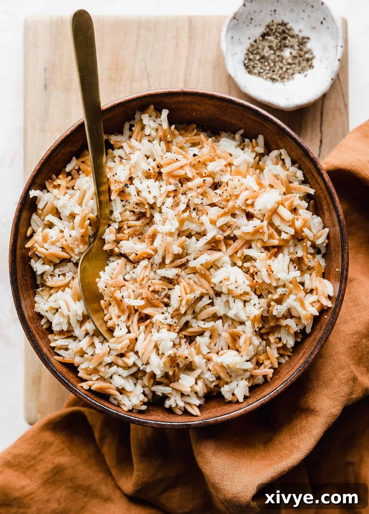 Orzo Pilaf 2 Golden Orzo Rice Pilaf served in an elegant brown bowl, resting on a rustic wooden cutting board, ready to be enjoyed.